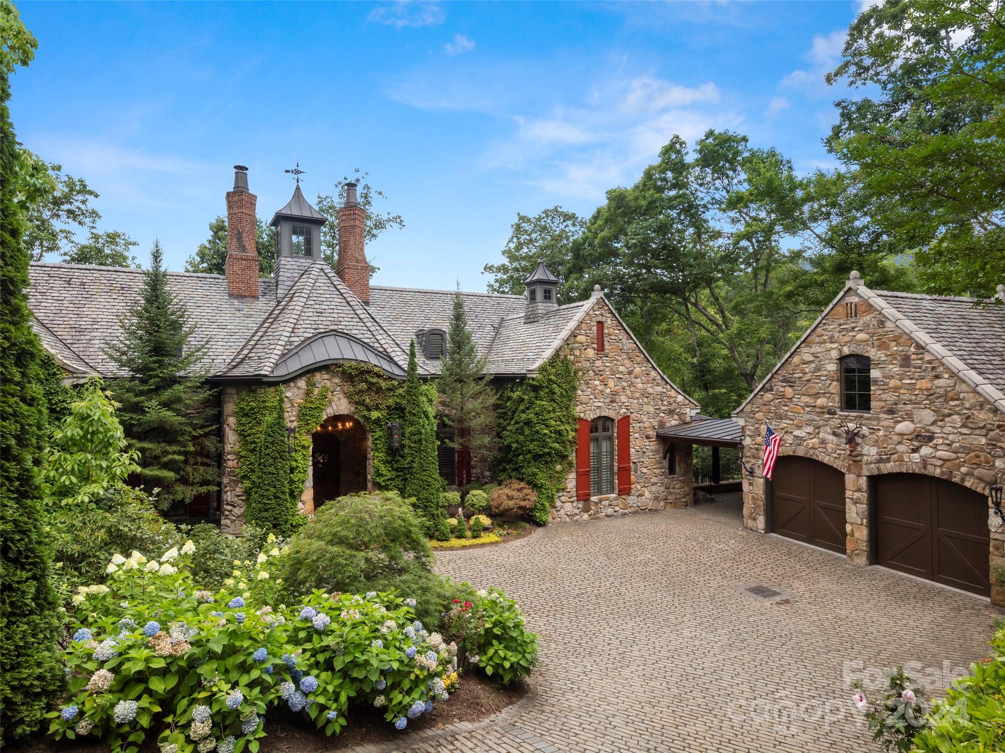 Welcome to Aslan Court, a unique luxury estate inspired by a 1920s English countryside hunting lodge. Designed by the renowned Los Angeles architect William Hablinski and meticulously crafted by Thompson & Brown Custom Builders. Filled with character and charm, you will be whisked back to a different time. This magical mountain hideaway invites you to step back in time while enjoying all the comforts of modern living. Nearly 100% American-made sourced materials contribute to its authenticity and quality. Whether you’re seeking a private retreat or a space to entertain guests, you’ll enjoy the two story great room with stenciled walls and limestone fireplace, the open kitchen equipped with top-of-the-line appliances, custom cabinetry, and charming breakfast room, or the wraparound covered deck that overlooks a peaceful waterfall feature. There is also a dramatic two-story library, main level primary suite, and even a cobblestone courtyard with gas lanterns and slate roof. It’s magic!