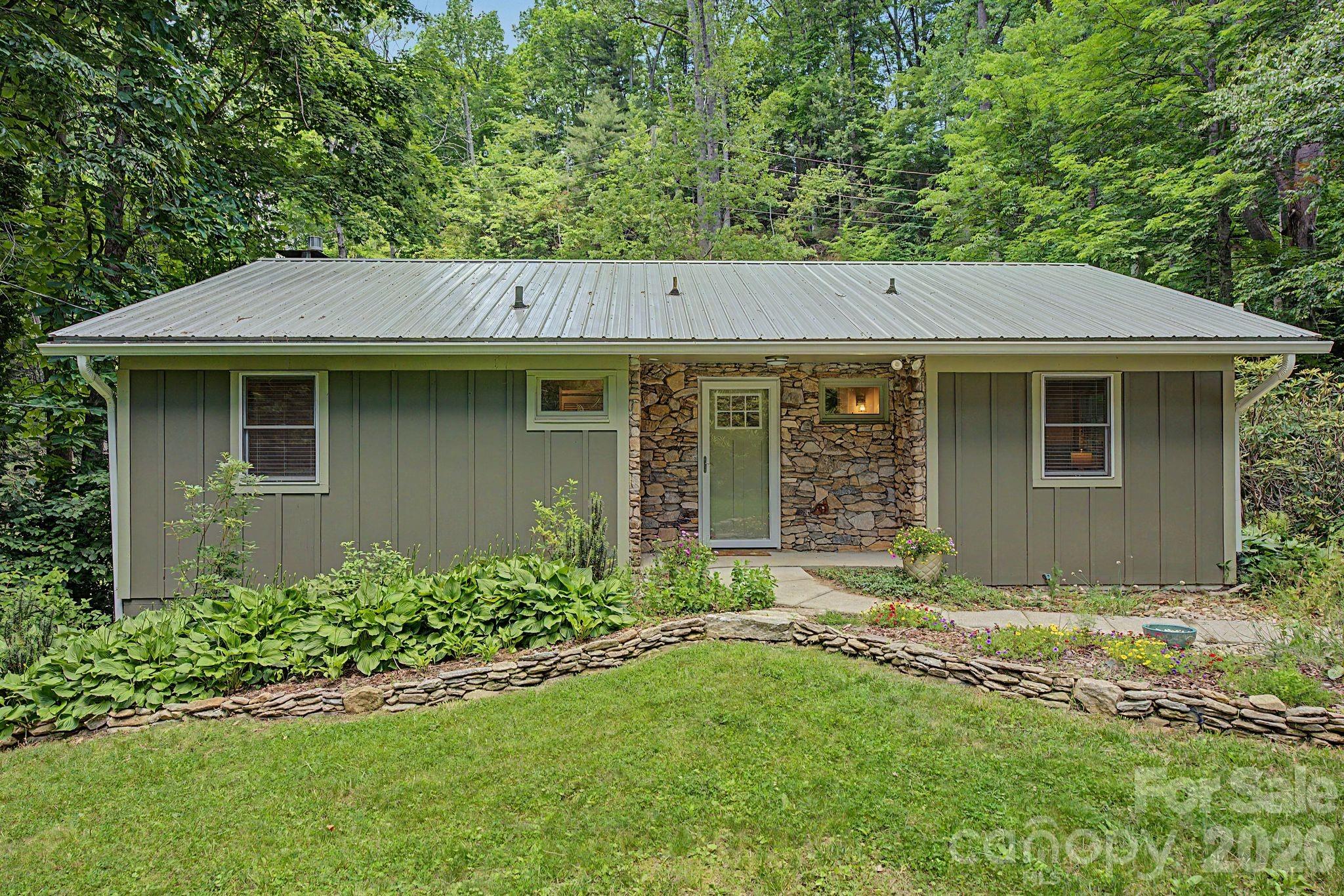 Discover the beauty of creekside living at 878 Garren Creek Road, a thoughtfully updated mountain cottage resting on 2.24 acres with more than 300 feet of frontage on both sides of Garren Creek. Surrounded by native landscaping, waterfalls, and the sounds of three creeks, this unique property offers privacy, charm, and natural beauty just minutes from Asheville. Designed for comfortable one-level living, the home features 2 bedrooms, 1.5 bathrooms, hardwood floors, custom trim work, and abundant built-in storage. The living room showcases a native stone fireplace with custom shelving, while the remodeled kitchen offers granite countertops, a pantry, and updated appliances, including a dishwasher and an induction range. The finished basement provides additional flexible living space with a Jøtul propane stove, recessed lighting, and oversized barn doors. A detached garage with its own HVAC system and electrical panel offers endless possibilities for a studio, workshop, office, or guest space.
Enjoy the outdoors from the Trex deck overlooking the creek or the covered flagstone patio below. Recent improvements include updated HVAC systems, plumbing components, a 200-amp electrical service, radon mitigation, a metal roof, and extensive landscaping. A rare opportunity to enjoy a peaceful mountain setting with modern updates and room for relaxing, creating, and exploring.