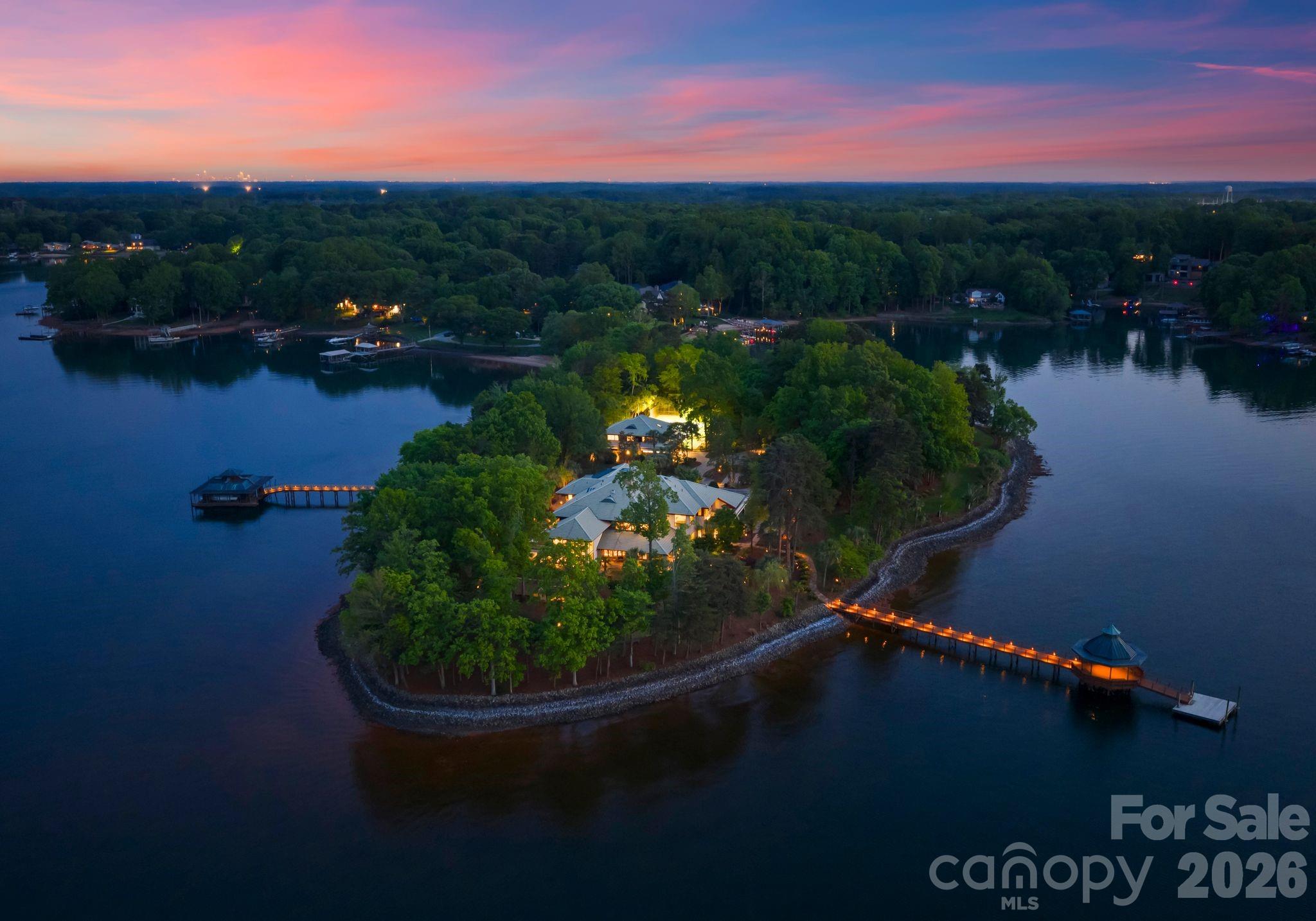 Designed by renowned architect Harry Schrader, Merancas Island is an extraordinary private island standing as one of the most significant residential offerings ever to come to market in the Carolinas. Spanning 4.5 pristine acres along Lake Norman’s shoreline, this estate delivers a resort lifestyle with no equal. Custom architectural details, bespoke lighting, and timeless design define every corner of the 14,317-square-foot residence. 

A gated entry winds through lush tropical grounds past palm trees, sculpture gardens, the guest house, and tennis court before arriving at the primary residence, where breathtaking lake views greet you from every room. A covered pavilion entry path flanked by a tranquil pond leads to curved doors with elegant colored glasswork, opening into a foyer of immediate distinction. Soaring 20-foot ceilings and a refined stone fireplace set the tone for the craftsmanship found throughout. Elevator access to the upper level and attic is positioned just off the entry hall.

The great room is the heart of the home, featuring a 25-foot ceiling, lake views on three sides, and expansive windows that dissolve the boundary between interior and exterior. A gas fireplace anchors the space as doors flow out onto multiple patios overlooking the water. The kitchen features a generous island, gas cooktop and ovens, granite countertops, and a full butler's pantry, all complemented by a sunny breakfast area with lake views. The dining room offers architectural ceiling details, a stone fireplace, and a custom light fixture by Schrader, with direct access to a screened outdoor patio. A dedicated wine room with stone finishes, custom racks, and glass display cabinetry sits nearby.

One of the home's most remarkable amenities is the enclosed indoor pool, clad in Tennessee Field Stone and cedar walls beneath a cedar ceiling with skylights and integrated plant walls. A full bath with sauna complements the pool area. Adjacent, a sun-filled flex room with plantation shutters and a glass wall peering into the pool space serves equally well as a bonus guest suite, office, or playroom. A private executive office features custom built-ins and a sliding panel connecting to the crafting room beyond, a generous creative space anchored by a large center island. Additional main-level spaces include a storage room, a full bath, a powder room, and a drop zone from the three-car garage.

The upper level is anchored by the exceptional primary suite, featuring a custom platform bed with integrated bookshelves, a fireplace, and a hidden bookcase door that opens to a reading loft with a spiral staircase to the great room, making this space genuinely one of a kind. The primary bath offers dual vanities, a soaking tub, a custom stone and wood shower, and two walk-in closets with glass display cabinets. A private terrace overlooks the water from the bedroom.
Two guest bedrooms offer lake views and an ensuite bath, served by an additional shared hall bathroom. The theater room delivers a full entertainment experience with a pool table, wet bar, and projector system. The children's playroom is a world of its own, a hand-painted mural wraps the walls and ceiling, built-in beds with trundles, and an adjacent wet room handles every art project and lake-day cleanup with ease.
The guest house offers a recently updated retreat with an open-concept living and kitchen area, two bedrooms, a shared bath, and its own three-car garage. Outside, stone walkways wind through the island, past a fenced tennis court, two docks with boat lifts and a covered gazebo, a sandy private beach, a shed, and a dog run. 

Ideally situated less than 30 minutes from Uptown Charlotte with convenient access to major roadways, Merancas Island places you at the heart of everything Lake Norman has to offer, from world-class dining, boating, waterfront recreation, to a vibrant social scene. This is lake living at its absolute finest.