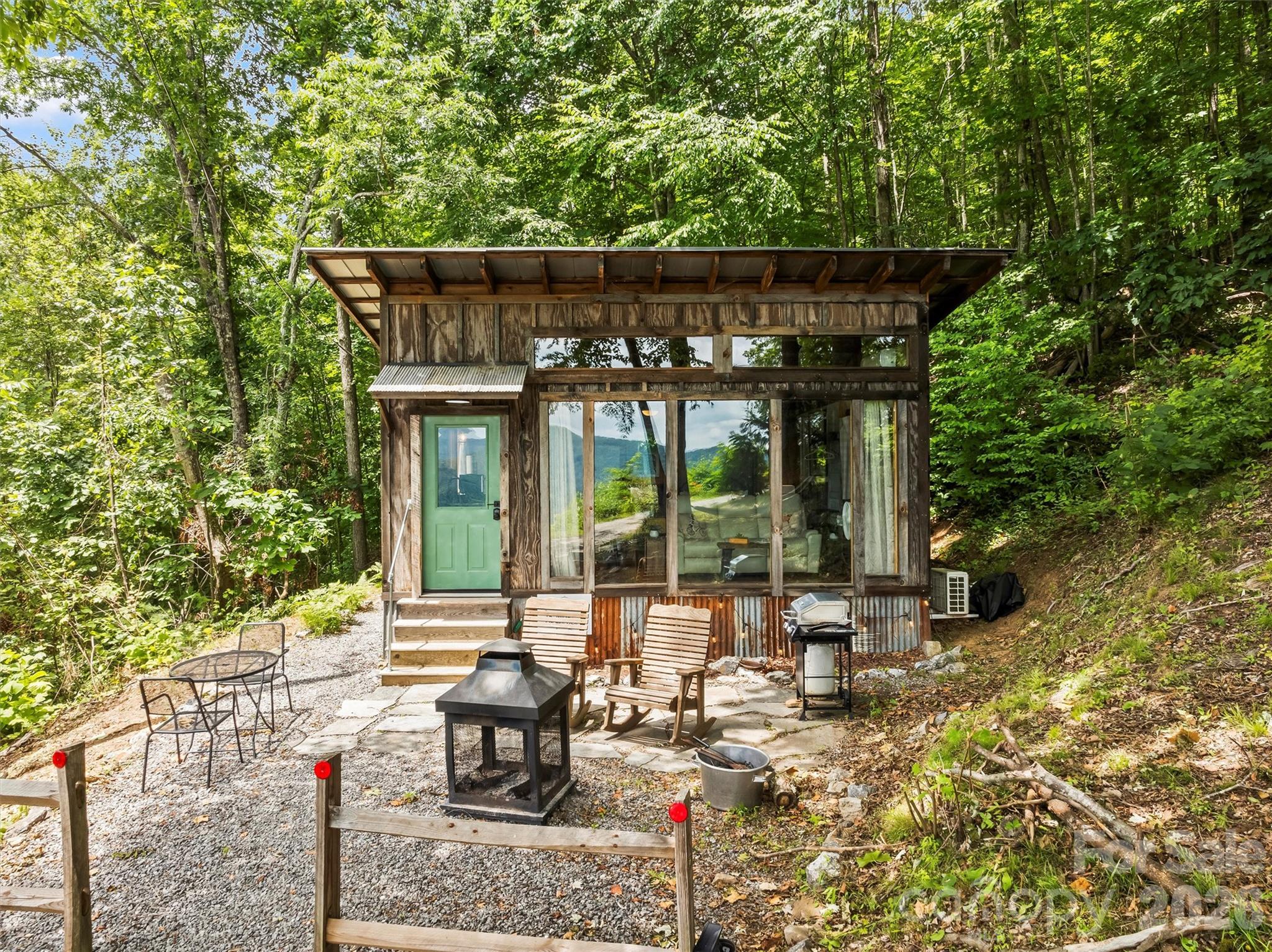 Set on a spacious lot with spectacular mountain views, this unique property offers an uncommon opportunity in Haywood County! The property features a nicely finished glamping home with an open concept floorplan and one bathroom. Relax on the front porch and take in the awe-inspiring views into the National Forest. The home is connected to electricity and has a functioning kitchen, mini split for HVAC, and is sold fully furnished with quality fixtures, furnishings, and linens. The seller is willing to discuss the possibility of installing a conventional septic system. Water is currently supplied by a roof collection system with a 1500 gallon storage tank, and water is treated through 3 phases of filters and a UV filtration process. This sizable lot offers another potential build site with the same excellent views to create your dream mountain home. +-2.3 acre portion of PIN offered with this listing. Come see this special property today! Seller is willing to install a septic field and connect to water. She will require an acceptable non-refundable deposit from the buyer. Home renovation was completed without pulling permits. Electrical permits were obtained.