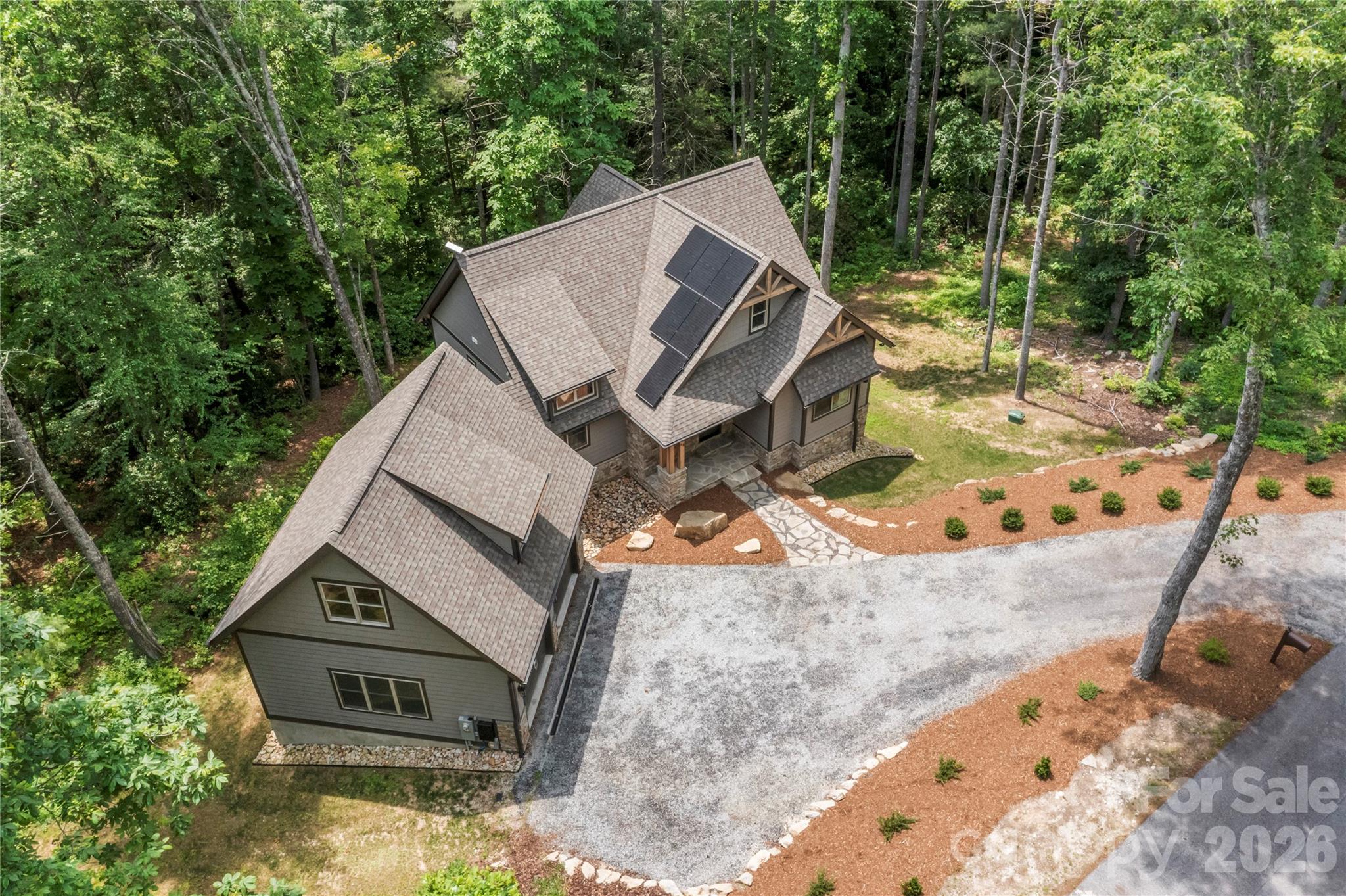 Discover serene mountain living in this nearly new home, ideally next to a green space in a sought-after WNC community. Enjoy rare privacy with a peaceful creek at the rear and direct access to scenic hiking trails. Inside, the open-concept main living area boasts soaring vaulted ceilings in the kitchen, living room and primary suite, creating a bright, airy atmosphere. A gas fireplace offers cozy ambiance. Gleaming hardwood floors and granite countertops flow throughout the main level. Two spacious covered decks, accessible from main living areas, invite relaxation amidst native trees and creek sounds. The fully finished basement provides additional bedrooms, living space and direct nature access. This home embraces sustainable living with solar panels, a Tesla Powerwall 3 for energy storage/backup, and an EV charging station. Enjoy vibrant community amenities including clubhouse, well-equipped fitness center, outdoor pool, recreational trails and stunning natural waterfalls. Seller offering credit for first year of HOA fees.