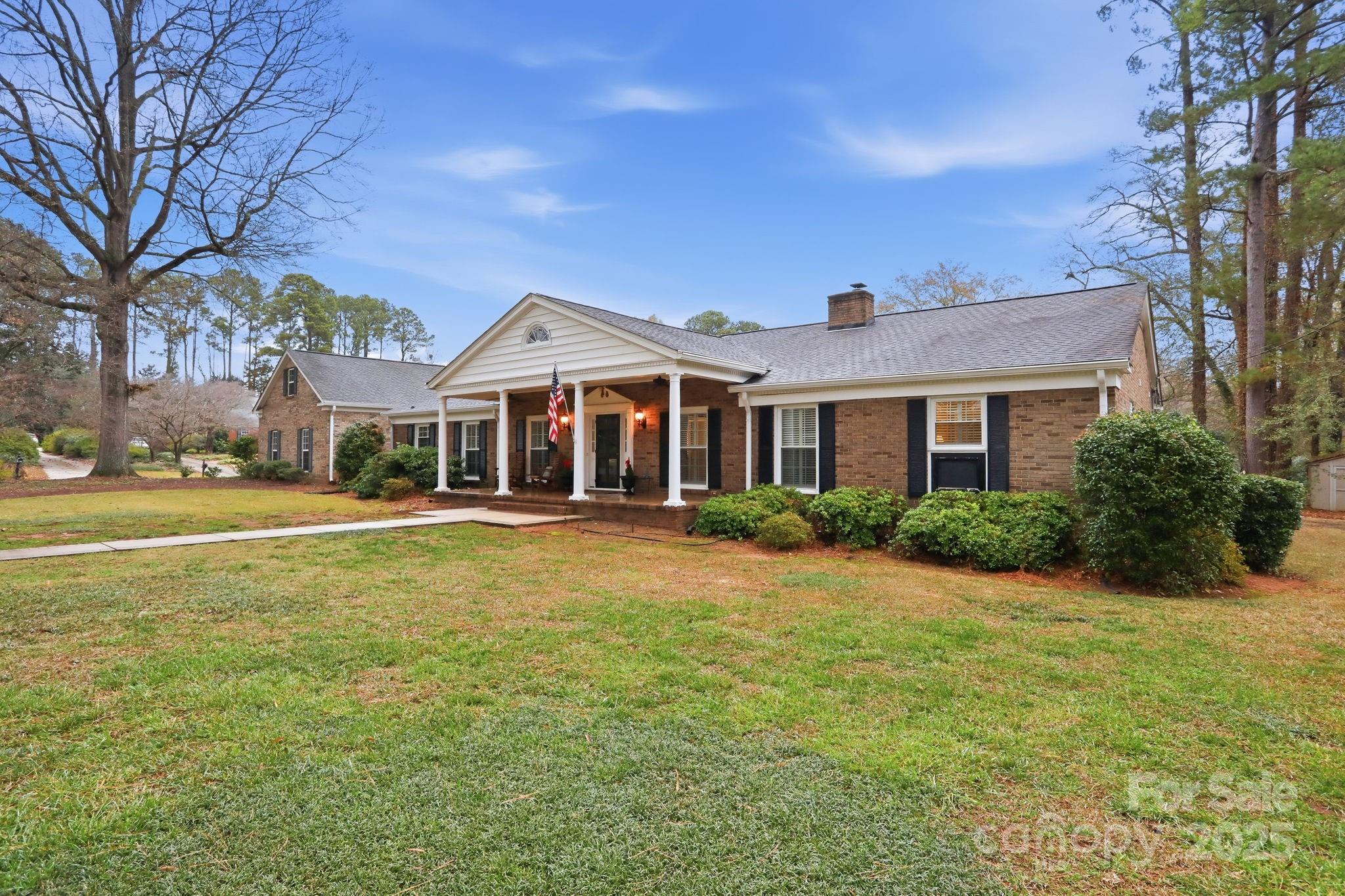 Elegant, updated and effortlessly livable, this 1965 full-brick traditional/colonial offers true single-level living in one of Rock Hill’s most established neighborhoods. Designed for comfort and privacy, the floor plan features two primary bedroom suites within a 4-bedroom, 3-bath layout. The den, kitchen and primary bath have been beautifully updated, with refreshed flooring and meticulous care evident throughout. Garden views frame both the covered front porch and the covered rear patio, overlooking a corner lot with mature trees and a partially fenced back yard. Surrounded by other substantial brick homes on generous lots, the setting feels quiet, refined, and well established. A versatile family room over the garage plus a detached garage add flexibility for work, hobbies, or guests. An ideal opportunity for discerning buyers seeking “forever home” quality on a single floor. We hope you will come visit.
