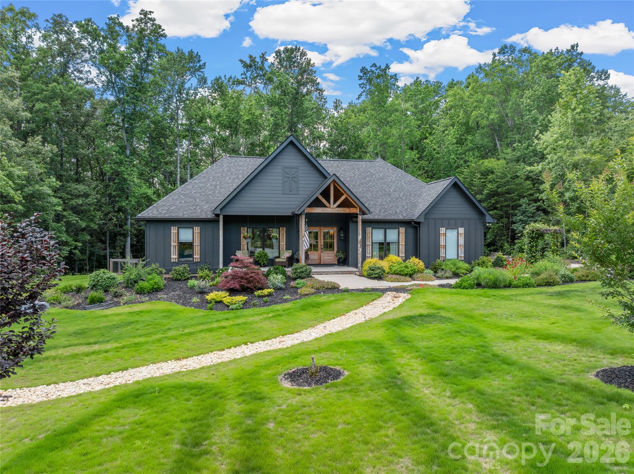 Custom built in 2023, this 4 bed, 3.5 bath modern farmhouse is move-in ready with high-end finishes at every turn. A long chipped slate driveway winds past professional landscaping, a charming garden path with pergola arch, and a striking dark board-and-batten exterior with timber frame entry — setting the tone for something special before you even step inside.
Inside, an open-concept main level unfolds with vaulted ceilings and a brick fireplace anchoring the great room.  The chef's kitchen is equally impressive — quartz countertops, a large knotty alder island, white shaker cabinets with wood accents, subway tile backsplash, and stainless professional-grade appliances. A dedicated laundry room continues the craftsmanship with knotty alder cabinetry and leathered granite counters.
The primary suite is a true retreat with a spa bath featuring a double quartz vanity, soaker tub, walk-in tile shower, shiplap accent wall, and a massive custom walk-in closet. Large glass doors off the main living area lead to a fully finished covered porch with wood-plank ceiling and mounted TV — the perfect extension of your living space.
Step outside to a fully fenced backyard with artificial turf — green, clean, and maintenance-free year-round. No mowing, no mud, no mess. 

Every detail thoughtfully considered, every finish carefully chosen. Some homes you settle for — this is the one you've been waiting for.