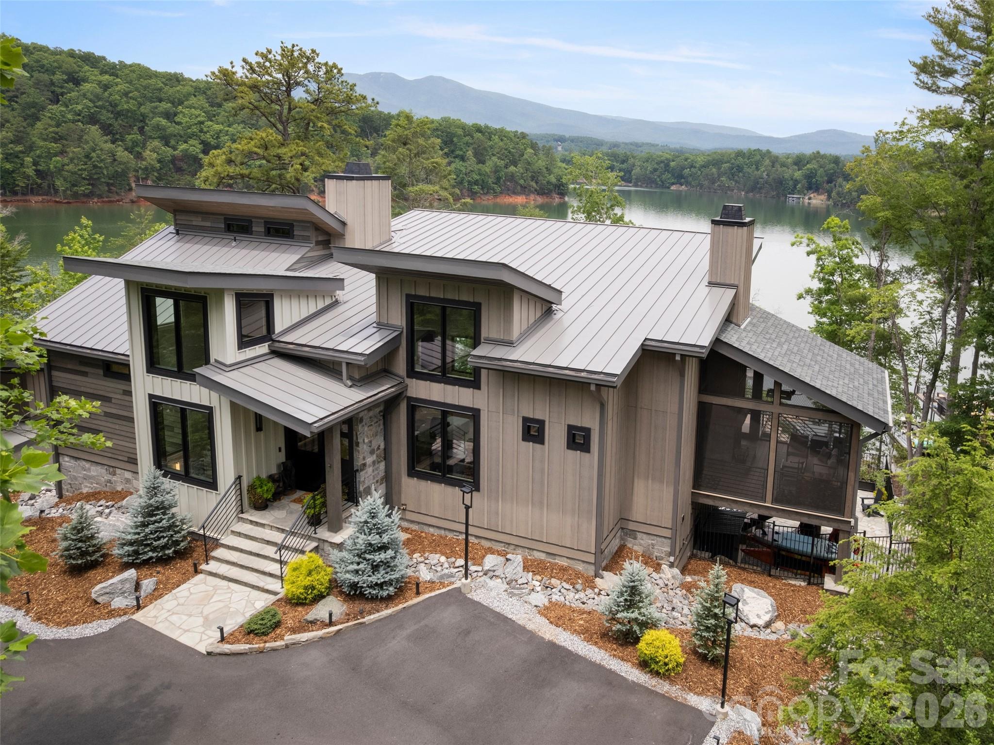 A masterful expression of mountain-modern luxury, this exceptional waterfront residence
in The Arbor at Lake James was crafted with an uncompromising dedication to quality and
detail. Sweeping lake and mountain vistas unfold from nearly every room, creating a
seamless connection to the surrounding landscape. Soaring wood-plank ceilings,
expansive walls of glass, wide-plank white oak flooring, custom alder cabinetry, live-edge
white oak accents, artisan ironwork, and dramatic floor-to-ceiling stone fireplaces create a
home that is both sophisticated and inviting. Perfectly positioned on 245± feet of private
shoreline, this newer custom-built retreat seamlessly blends contemporary luxury with the
natural beauty of waterfront living. The chef's kitchen is a showcase of exceptional design
and function, featuring Bosch 800 Series appliances, quartzite countertops, a hidden walk-in pantry and a custom live-edge white oak island. The private primary suite offers a spa-inspired bath, premium finishes and a covered lakeside deck designed for peaceful
mornings and stunning sunset views. Constructed with exceptional attention to detail and
designed for both luxury and longevity, the residence features premium materials,
advanced climate-control systems, a whole-home generator, integrated security, EV
charging capability, and thoughtfully selected upgrades that provide comfort, efficiency,
and peace of mind. Every element reflects an unwavering commitment to quality,
craftsmanship, and enduring value. Outdoor living is equally impressive with a screened
lakeside porch featuring a stone fireplace and built-in heater, an expansive entertaining
deck, boulder fire pit, mature landscaping, and a gentle stone pathway leading to the
water's edge. A deep-water double-deck dock with HydroHoist boat lift provides immediate
access to the crystal-clear waters of Lake James. Offered fully furnished and including the
boat, dock, and lift, this extraordinary turnkey property presents a rare opportunity to enjoy
one of Lake James' finest waterfront lifestyles from the moment you arrive!