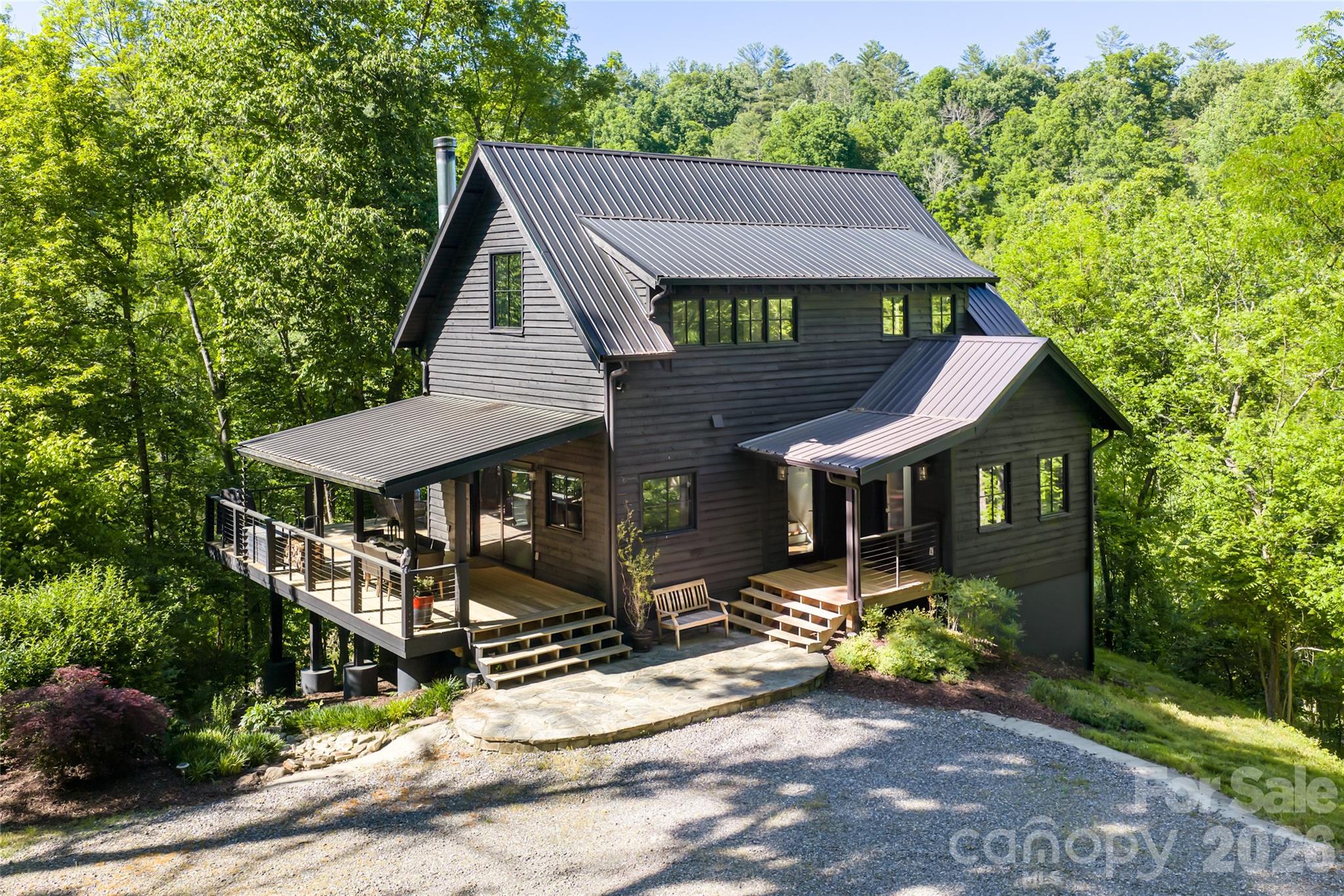 Set upon a private stretch of wooded acreage just across from the storied waters of the Ivy River, this elegantly rustic A-frame retreat offers a rare harmony of architectural character and natural splendor. Here, mornings begin with mist rising from riverbanks and the promise of world-class fly fishing just near your door. A generous side porch welcomes you home, while a classic front porch and expansive rear deck create a seamless dialogue between indoors and out. From the deck, tranquil river views and gentle murmur of flowing water form a captivating backdrop for alfresco dining or quiet reflection beneath a canopy of trees. Inside, wide shiplap walls and warm wooden floors evoke timeless craftsmanship. The soaring vaulted ceiling in the living room amplifies light and volume, while ample windows frame the surrounding woodland like living works of art. At the heart of the home, a striking fieldstone fireplace rises dramatically to the ceiling, an architectural anchor and gathering place that radiates warmth and authenticity. The open kitchen and living area are designed for convivial entertaining and intimate evenings by the fire. An efficient gourmet kitchen features a gas cooktop, farmhouse apron sink and thoughtful appointments that balance rustic charm with modern convenience. The main level offers a serene en-suite bedroom and bath, providing ease and privacy. Upstairs, an additional en-suite bedroom creates a peaceful retreat among the treetops, where vaulted lines and filtered light enhance the sense of escape. The lower level reveals a versatile recreation room, enjoyed as a bunk room, alongside a full bath and utility room, offering flexible space for guests, hobbies or relaxation after a day on the river. Outdoors, a dedicated fire pit area invites evenings beneath the stars, where stories are shared and embers glow against the woodland twilight. A haven of texture, warmth and natural beauty, this A-frame sanctuary captures the essence of refined mountain living, private, poetic and positioned for life along the river. House is being sold furnished.