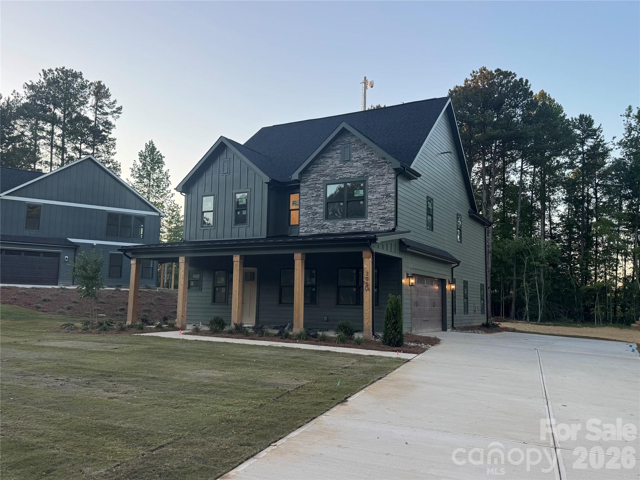Welcome to 205 Parkdale Drive, a beautifully designed new construction home in Belmont offering 4 bedrooms, 3 full baths, and 2,986 square feet of thoughtfully crafted living space on a generous 0.56-acre homesite. Located approximately one mile from downtown Belmont, you’ll enjoy convenient access to local shops and dining. The exterior showcases James Hardie lap and board-and-batten siding in Pewter Green, accented by Centurion Grey ledgestone and rustic black architectural shingles for a timeless yet modern curb appeal. A covered front porch creates a warm and inviting entrance, while the rear covered porch provides the perfect space for outdoor entertaining or relaxing evenings at home. Inside, a light and airy palette sets the tone with Pure White walls, crisp trim, and cove crown moldings. Hand-scraped engineered hardwood floors flow throughout the main living areas, adding warmth and character. The two-story layout offers a functional and flexible design, including a main-level primary suite along with an additional bedroom and full bath ideal for guests or a home office. The kitchen serves as the heart of the home, featuring white shaker cabinetry, glass-front upper cabinets with LED lighting, quartz countertops including a striking Sahara Quartz island and Marengo Quartz perimeter surfaces, and a classic white subway tile backsplash. A KitchenAid appliance package and chrome Moen fixtures complete this beautifully appointed space. The family room centers around a ledgestone fireplace with a cedar mantle, and upgraded iron balusters enhance the architectural detail of the staircase. The primary suite offers a spa-inspired retreat with quartz countertops, white shaker cabinetry, framed mirrors, chrome fixtures, and a tiled shower finished in matte porcelain with basketweave accents. With a two-car attached garage, quality finishes throughout, and a prime location just minutes from the heart of Belmont, this home perfectly blends style, comfort, and convenience.
