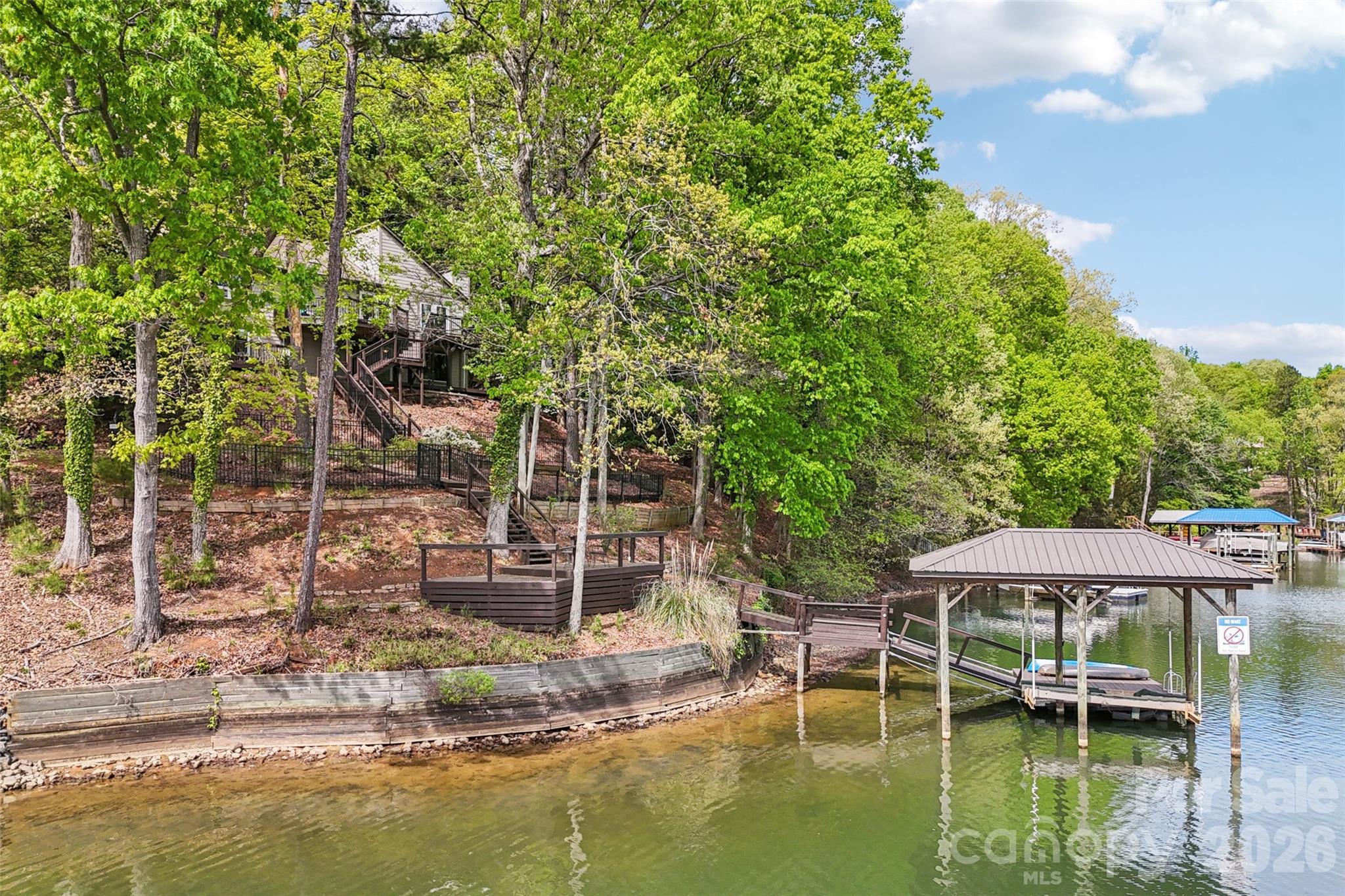 Situated on a waterfront wide cove lot off the heart of the main channel, this Tega Cay beauty perfectly combines modern updates with mid-century charm.  Hardwood floors on the main level unite the open concept floor plan. The vaulted ceiling great room is filled with natural light and flows seamlessly to the dining room and kitchen.  Kitchen has been remodeled and included ample cabinets, granite counters, bar top dining and tile backsplash.  Primary suite on the main has year round water views, updated en suite bath, sitting room and walk-in closet.  Generously sized secondary bedroom on main   has hallway access to updated bath.  Venturing downstairs the second primary suite awaits and features year round water views, double walk-in closets and updated bath.  Huge flex space in basement with fireplace plus entertaining bar and bonus room.  Relax on either the upper or lower decks overlooking the fenced backyard.  Walk down to your private dock complete with covered boat lift.  Conveniently located in Tega Cay moments from the golf club with award winning school assignments, this is the lake life home you have been waiting for!