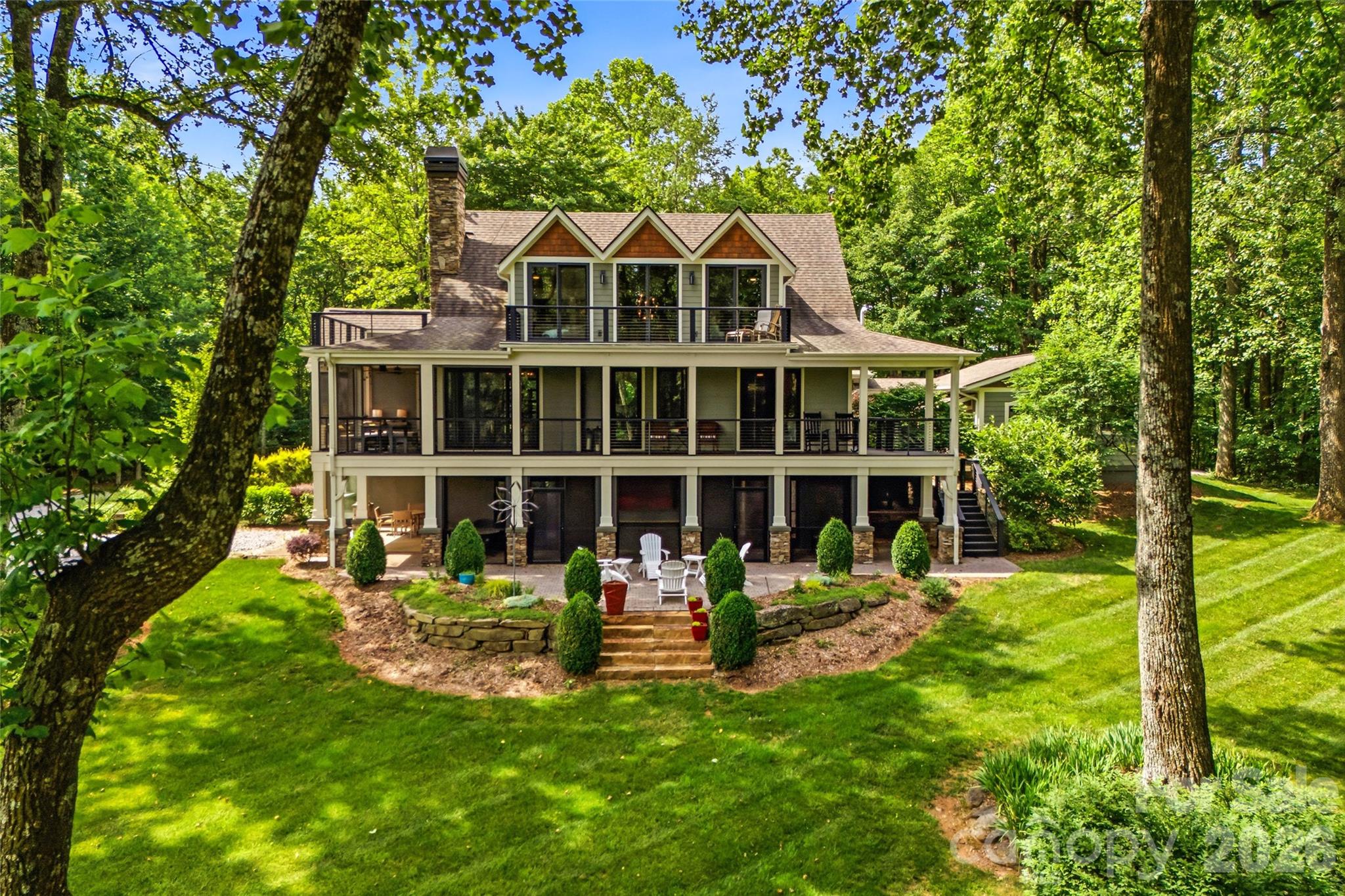 Welcome to 233 Tanglewood Lane, a truly rare and private mountain retreat in the desirable Lake Sheila neighborhood of Saluda, North Carolina, offering residents access to a beautiful crystal blue lake and all the non-motorized recreation it provides. Nestled on more than three pristine acres, this exceptional property offers breathtaking mountain views from the home, creating a stunning backdrop in every season. Bordering an incredible 30,000 acres of protected watershed land, the property provides unparalleled privacy, abundant wildlife and a lifestyle that is increasingly difficult to find. This beautiful home features three spacious ensuite bedrooms, along with two additional bonus rooms currently being utilized as bedrooms, providing ample space for family and guests. The thoughtfully designed interior showcases a stunning chef’s kitchen, complemented by custom stonework that flows throughout the home, adding warmth, character and timeless craftsmanship. A custom-built, temperature-controlled detached garage offers the perfect space for car enthusiasts, hobbyists or additional storage, providing year-round comfort and versatility to complement this exceptional property. Gather around the indoor wood-burning fireplace on cool mountain evenings or enjoy cozy nights beside the outdoor porch fireplace while taking in the peaceful surroundings. Expansive open living spaces, inviting decks and covered porches create a setting for entertaining or simply relaxing and enjoying the beauty of nature. A folding glass wall system seamlessly connects the main living area to the screened porch, creating an exceptional indoor-outdoor living experience. Whether enjoying cool evenings by the fire or relaxing on breezy afternoons, you will love this space. Outside, the meticulously manicured lawn and landscaped grounds enhance the property’s charm. A utility shed and separate access road provide convenient storage and easy access for off-road vehicles, lawn equipment or recreational use. Located only minutes from charming downtown Saluda, this extraordinary property offers the perfect balance of privacy, recreation and convenience. With its rare combination of mountain views, acreage, protected surroundings, lake access, exceptional craftsmanship and proximity to town, 233 Tanglewood Lane is a unicorn property and a once-in-a-lifetime opportunity.