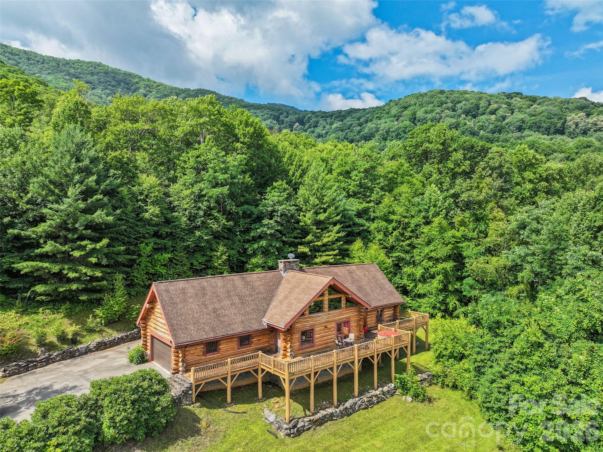 Discover this extraordinary log home estate in the serene Balsam area of the Blue Ridge Mountains, Waynesville, North Carolina. Nestled on over 4 pristine acres at an impressive 3,740-foot elevation, this custom-built retreat offers breathtaking, year-round long-range mountain views that stretch for miles. Adjoining thousands of acres of protected Blue Ridge Parkway lands, the property delivers unparalleled privacy and natural beauty. A massive white pine log home sourced from Virginia stands proudly, complemented by elegant dry-stack stone accents that blend seamlessly with the surrounding mountain landscape. Just off a state-maintained road via a private drive, the concrete-and-gravel driveway leads to a lovely, level front yard that gently rolls up to the home site, creating the feel of a private mountain estate. The main level welcomes you with an open, light-filled layout centered around a soaring 20-foot cathedral ceiling in the living room—perfect for gathering and soaking in the panoramic vistas. The spacious eating kitchen area features a wood-burning fireplace that has never been used, ready for your personal touch and cozy evenings. Adjacent, the luxurious primary bedroom suite boasts a vaulted ceiling, an oversized walk-in closet, and a spa-like bath complete with a jet tub, walk-in shower, and dual vanity. Additional main-level conveniences include a dedicated home office area, a powder room, and a large laundry room. Upstairs, two generous secondary bedrooms each feature a large walk-in closet and share a convenient Jack-and-Jill bathroom. The unfinished basement level offers excellent potential, with space planned for a family room featuring a fireplace and wood stove, a functional bath, and a tandem garage for ample storage and parking. Step outside to enjoy the expansive front uncovered deck and the rear covered deck—ideal spaces for morning coffee with the sunrise over the mountains or evening entertaining under the stars. Architectural shingles top the roof, ensuring durability in the mountain climate, while the well and septic systems support low-maintenance living. This rare offering combines timeless craftsmanship, modern comforts, and an unbeatable location in the heart of Western North Carolina’s Blue Ridge Mountains. Whether you seek a full-time residence, weekend getaway, or private sanctuary, this log home estate captures the essence of mountain living at its finest. The house has several deferred maintenance items, and the list price reflects those.