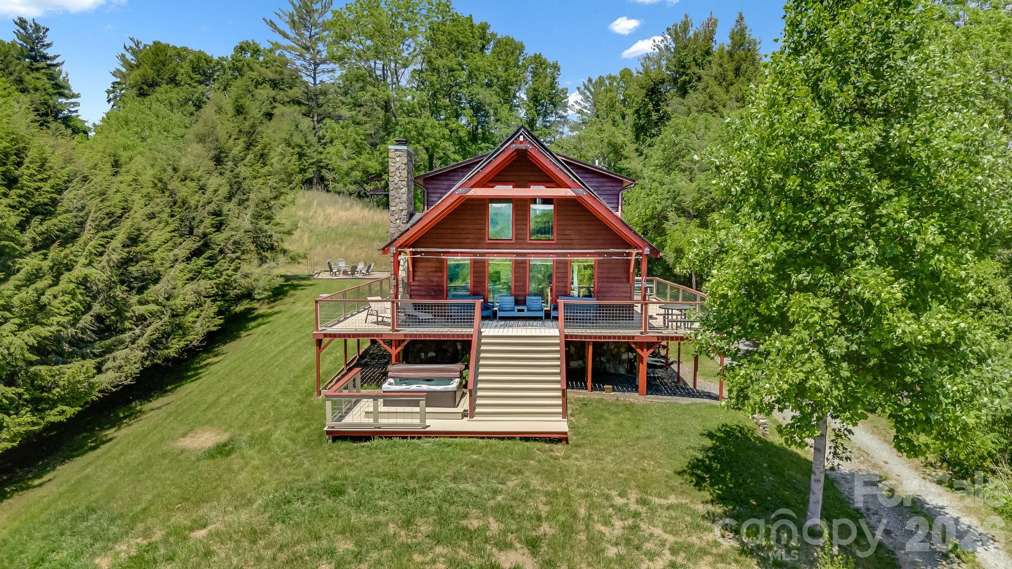 Nestled on a knolltop in beautiful Madison County, close to magical Marshall, this charming mountain retreat offers stunning year-round views, privacy, and the perfect blend of rustic charm and modern comfort. Escape to your private sanctuary, or in minutes, find yourself strolling down Marshall's main street full of local restaurants, distinctive art galleries, and cozy coffee shops.

Step inside to an airy, open-concept floor plan defined by soaring vaulted wood ceilings, warm wood accents, and massive prow-front windows that perfectly frame your year-round mountain views. The heart of the home features a cozy living room anchored by a classic wood-burning fireplace and a central kitchen island, ideal for casual morning coffee or evening entertaining. The main level hosts a comfortable bedroom and full bath, while the upper level is dedicated to a peaceful primary loft oasis. A private, multi-functional bonus room, perfect for a guest space, home office, media den, or creative studio, is located in the partly finished basement with both inside and walk-out access. 

Outside, extensive decking, a hot tub, a fire pit area, and a spacious yard create the ideal setting for entertaining, relaxing, or enjoying peaceful mountain evenings under the stars. Watch the sun rise over the ridgetops, spot deer and wild turkey crossing the yard, or watch the neighbors' cows graze peacefully at the distant fence line.

For the investor, this property is incredibly low-maintenance and highly practical. It features a massive three-car garage space (perfect for a game room or ping-pong setup), an abundance of driveway parking that can easily accommodate an RV, and a dedicated, locked supply room in the basement. Operated as a successful, part-time, rave-reviewed short-term rental, "The Outpost” is a rare find located just 5 to 8 minutes from Marshall, 10 to 15 minutes to Weaverville, and less than 20 minutes from Asheville. Come and see why Marshall is affectionately called "Magic Town"!