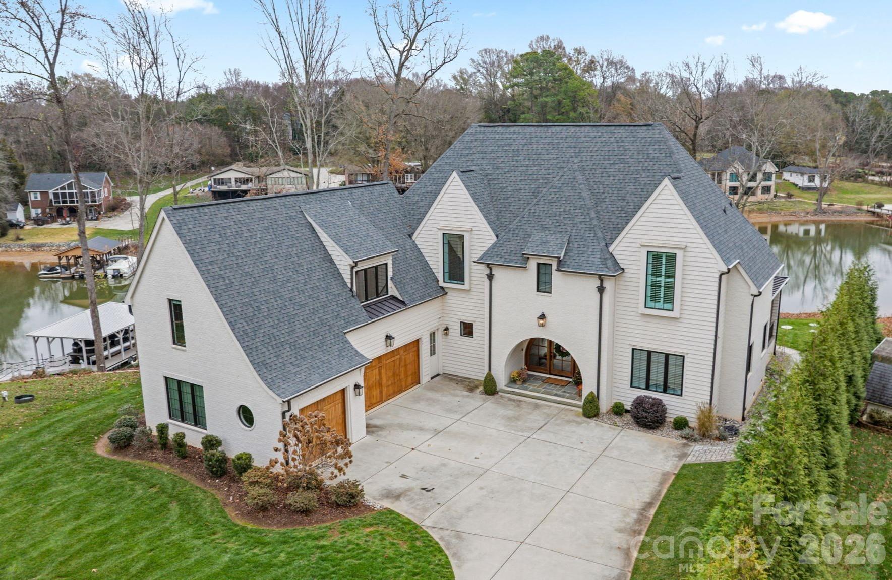 Welcome to an extraordinary waterfront retreat where refined modern design meets timeless sophistication on Lake Norman. This stunning 4,282 sq. ft. custom residence built in 2020 has been meticulously maintained. Offering 4 bedrooms, 4.5 baths, a private guest suite on the main level (perfect for guests or multi-generational living) and luxurious living spaces that seamlessly embrace the lake lifestyle. Step inside the dramatic arched doorway and be greeted by an open-concept main level bathed in natural light, and windows that frame sweeping lake views. Enjoy the comfort of your living room as the gas log fireplace offers warmth and built ins for added storage convenience.  The kitchen is a masterpiece with a Bertazzoni gas range, expansive quartz island with seating, sleek cabinetry, a wet bar, and a generous walk-in pantry — perfect for entertaining and everyday living. Expansive accordion glass doors open from the living areas to the covered screened patio, effortlessly combining indoor and outdoor living. The primary suite is a tranquil sanctuary, boasting vaulted ceilings, uninterrupted lake views and a spa-inspired bath. Two additional bedrooms with private bathrooms and a huge versatile bonus room deliver space and flexibility. The dedicated upper laundry room offers built-in storage, a sink and tile flooring. Step outside to your private outdoor haven featuring a covered patio with a gas log fireplace, ideal for year-round gatherings, and a sprawling yard with space for a future pool.  A peaceful stone pathway leads down to your waterfront with a covered dock including a hydro hoist boat lift plus a secondary cable lift ready for lake adventures. With a 3-car attached garage and no HOA, this residence blends luxury, convenience and recreation effortlessly. Stunning water views, premium finishes and thoughtful architectural details. Located minutes from premier dining, shopping, marinas, golf, parks and top-rated schools, this Lake Norman gem defines elevated waterfront living.