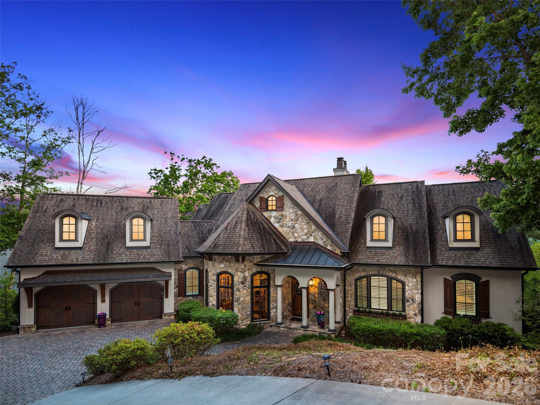 Situated within the prestigious gates of The Cliffs at Walnut Cove, this refined mountain residence presents a perfect harmony of elegant design and natural tranquility. The home’s exterior combines classic stone and stucco with arched timber accents, creating a timeless and inviting presence. Inside, the grand living room impresses with soaring vaulted ceilings, heavy timber beams, and a floor-to-ceiling stone fireplace. Large, expansive windows offer sweeping views of the lush mountain canopy, highlighting the home's exceptional privacy and peaceful, high-altitude setting.

The kitchen is a masterfully crafted culinary space, featuring a substantial island that serves as the epicenter for social gatherings. A professional-grade range is elegantly framed by a custom stone arch, while a sleek pass-through window facilitates an effortless flow for high-end entertaining. This sophisticated feature connects the interior to the screened porch, a private sanctuary with its own stone fireplace, perfect for hosting guests against the backdrop of cool mountain air. Also located on the main level is a versatile flex space, distinguished by a handsome coffered ceiling, that easily serves as a quiet home office or hobby room. The primary suite is a true retreat, featuring its own elegant coffered ceilings, a grand dressing room with a center island and custom storage, and a spa-like bathroom equipped with a large freestanding soaking tub and a spacious separate shower.

A stunning stone-walled staircase with custom wrought iron railings leads to the lower level, a dedicated space for relaxation and guest comfort. This level centers around a sprawling family room with rich timber beams and a second fireplace. The adjoining bar area is beautifully executed with warm wood textures and rustic stonework that echo the home’s European influences. Complementing this entertainment space is a wine cellar tucked behind an arched timber door, offering a refined element for social gatherings and quiet evenings alike. Two additional guest suites on this level provide private accommodations, each complete with its own bathroom and walk-in closet. Outside, the lower deck features a built-in hot tub area, while a stone fire pit in the yard offers a serene place to gather under the stars.

Residents of The Cliffs at Walnut Cove enjoy an unparalleled lifestyle centered around an 18,000-square-foot wellness center, indoor and outdoor pools, and a luxury spa. The community, which borders the Pisgah National Forest, is home to a Jack Nicklaus Signature golf course and "The Tavern," a vibrant social hub for fine dining. Located just minutes from the Blue Ridge Parkway and the cultural attractions of Asheville, this property offers a rare opportunity to enjoy mountain privacy with convenient access to the region’s premier recreational and cultural amenities.