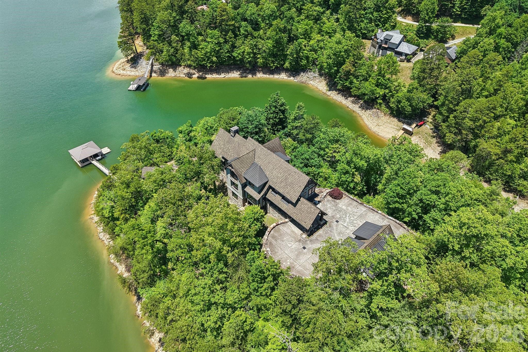 A truly exceptional lakefront legacy estate, this remarkable handcrafted mountain retreat is set on its own private peninsula within the prestigious gated community of Fontana Lake Estates. Surrounded by the crystal-clear waters of Fontana Lake and framed by the breathtaking backdrop of the Great Smoky Mountains, this extraordinary property offers a rare combination of luxury, privacy, craftsmanship, and adventure in one of Western North Carolina’s most sought-after waterfront destinations.

Thoughtfully designed for both grand entertaining and intimate mountain-lake living, the residence spans over 8,800 square feet of beautifully curated living space with seven bedrooms, multiple gathering areas, expansive outdoor living spaces, and timeless architectural details throughout. Rich wood tones, soaring timber frame construction, natural stone accents, and walls of glass create a warm yet dramatic atmosphere that perfectly complements the surrounding landscape.

The heart of the home is a stunning gourmet chef’s kitchen designed for hosting family and friends after long days on the lake. Multiple dining and living spaces flow seamlessly together, offering both comfort and sophistication. The great room features soaring ceilings, impressive beams, and panoramic views that immediately draw your attention to the sparkling waters beyond. Large windows throughout the home invite natural light inside while framing ever-changing mountain and lake vistas from nearly every room.

Designed with effortless indoor-outdoor living in mind, the home opens onto expansive covered terraces, lakeside decks, screened gathering spaces, and outdoor entertaining areas ideal for enjoying cool mountain evenings, spectacular sunsets, and peaceful mornings overlooking the water. Whether hosting large family gatherings, corporate retreats, or quiet weekends away, this property was created to accommodate unforgettable experiences.

The residence includes seven spacious bedrooms and multiple private guest suites, allowing family and visitors to enjoy comfort and privacy throughout their stay. Additional features include an elevator, fitness room, recreation and game areas, multiple fireplaces, generous storage, and beautifully integrated custom details throughout the home.

Outside, the property continues to impress with professionally designed landscaping, gentle access to the shoreline, and a private double-slip boathouse providing direct access to one of the cleanest and most scenic lakes in the Southeast. Fontana Lake is known for its emerald-green waters and more than 90% protected shoreline bordered by the Great Smoky Mountains National Park and Nantahala National Forest, preserving the natural beauty and serenity of the area for generations to come.

Located within the socially active wilderness community of Fontana Lake Estates, owners enjoy a unique mountain-lake lifestyle with access to community amenities, hiking trails, marina access, and a welcoming community atmosphere that blends luxury living with outdoor adventure. Residents gather year-round to enjoy boating, paddleboarding, fishing, hiking, and the unmatched beauty of the Smoky Mountains.

Conveniently located near Bryson City, the property is also just minutes from many of Western North Carolina’s most beloved attractions including the Great Smoky Mountains National Park, Nantahala Outdoor Center, Appalachian Trail, Deep Creek, scenic mountain railways, whitewater rafting, fly fishing, and countless outdoor recreation opportunities.

This is more than a home — it is a rare and irreplaceable mountain-lake estate designed to create generations of memories. Combining extraordinary craftsmanship, unmatched waterfront setting, and the lifestyle so many seek but few ever find, this iconic Fontana Lake property represents one of the region’s finest luxury offerings.