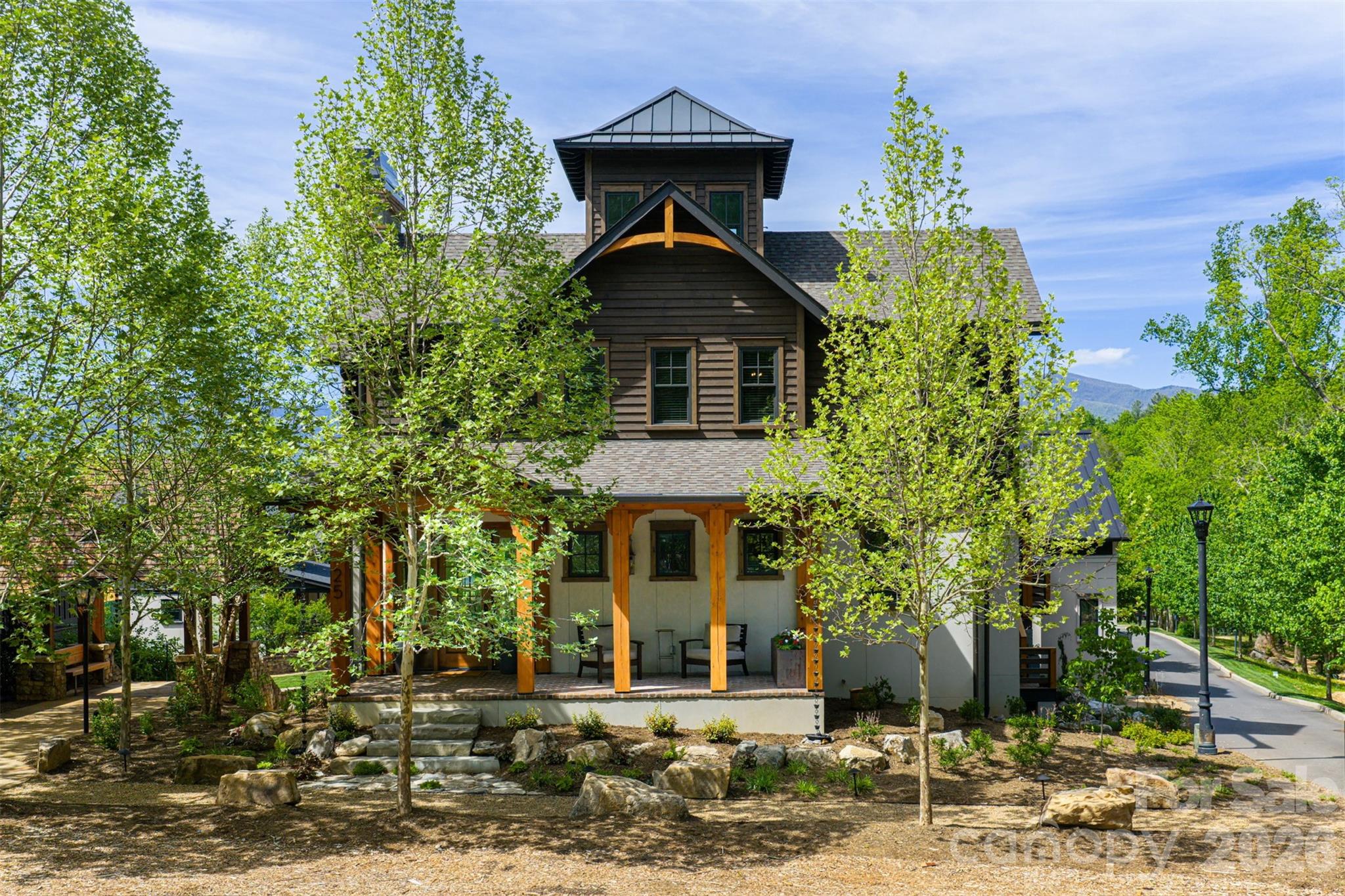 The Kingston – A Legacy Mountain Retreat

25 Rantis Lane | The Jacobs Cottages at The Village of Cheshire

Perched on a premier corner homesite just steps from storybook walking paths and meandering mountain streams, The Kingston is a rare union of timeless craftsmanship, grand scale, and unforgettable Blue Ridge Mountain views. Offered furnished, this custom residence spans over 6,000 total square feet of curated living space and rises into a signature King’s Tower with panoramic vistas of the Great Craggies and the Seven Sisters.

From the moment you arrive, gas lanterns glow against rich Western Red Cedar timber framing, welcoming you onto a covered brick front porch that feels pulled from another era. Inside, wide-plank hardwoods, shiplap detailing, reclaimed oak accents, and five fireplaces create warmth and authenticity at every turn.

Designed for gathering as beautifully as it is for retreat, the main level opens into an airy kitchen and living area anchored by a wood-burning fireplace. Step onto the covered rear deck to experience long-range mountain views beside an outdoor hearth. A butler’s pantry, mudroom, dog station, and private guest suite—with its own living room, kitchenette, laundry, fireplace, balconies, and deck—offer luxury and flexibility for hosting.

Upstairs, three bedrooms and a study accompany a show stopping primary suite where sunrise spills across the mountains. Enjoy a spa bath with soaking tub, walk-in shower, and generous custom wardrobes with built-ins and a window seat perfectly placed for quiet moments above the valley. A conveniently located washer and dryer just outside the primary suite adds everyday ease without compromising elegance.

The walk-out terrace level is made for celebration and relaxation alike: media and game spaces, an indoor/outdoor bar, sauna, additional bedroom and full bath, a dedicated laundry room, and fireplaces that extend the experience outdoors to a covered brick terrace.

And crowning it all, the King’s Tower—an inspiring aerie to take in the full sweep of the kingdom below.

5 Bedrooms | 5.5 Baths | Elevator | 2-Car Garage | Furnished

Whether envisioned as a full-time residence or an heirloom mountain escape, The Kingston delivers elevated living in the heart of one of Western North Carolina’s most beloved communities.

Owner/Broker/Developer Property