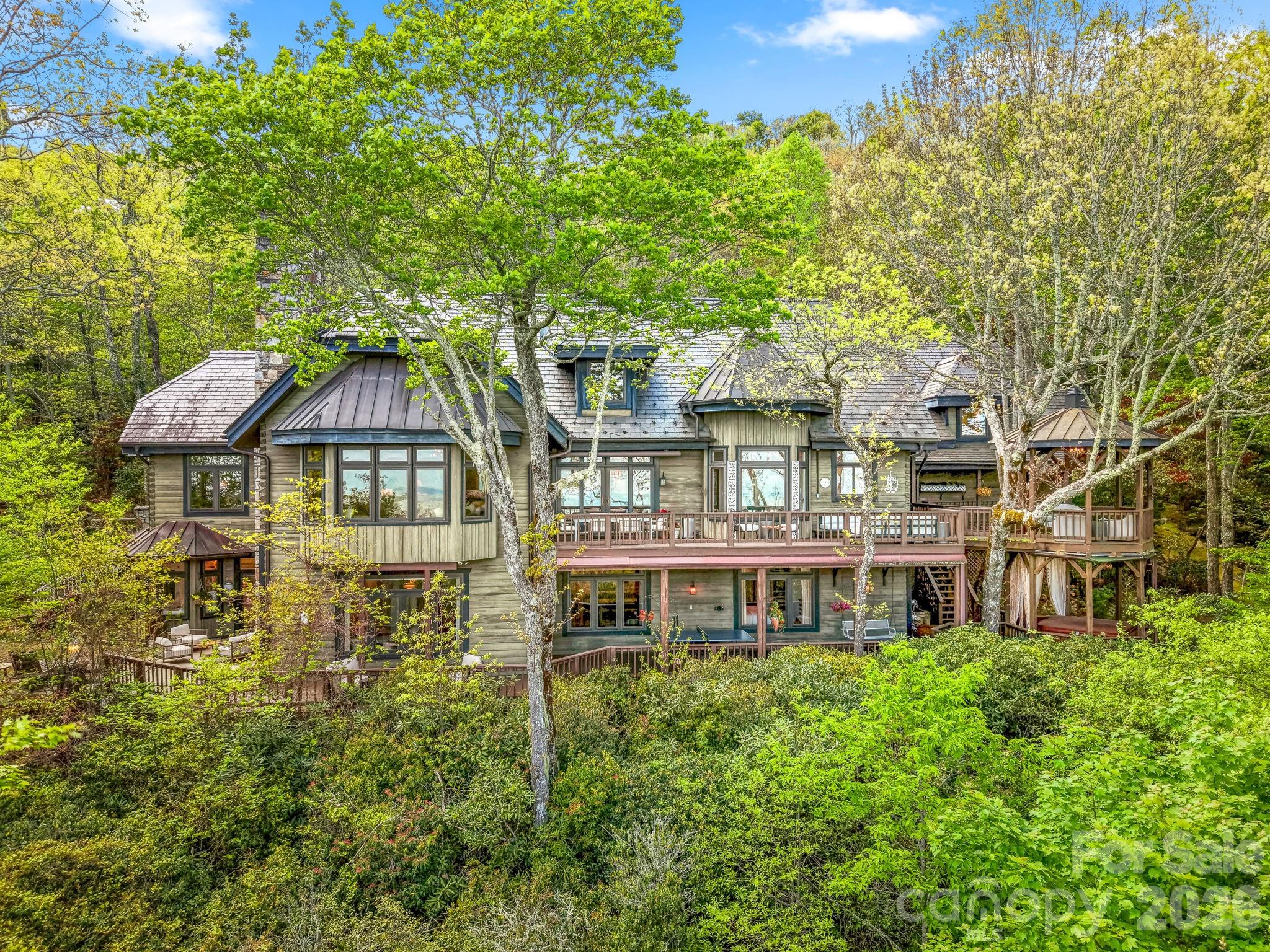 Some homes are impressive; others are unforgettable. Nestled within the highly sought after Lake Toxaway Estates, in the heart of the Blue Ridge Mountains—where the Land of Waterfalls meets refined luxury—this private sanctuary feels like a destination few will ever discover. Inspired by the charm of an English countryside lodge, the home blends old-world character with modern turnkey elegance featuring handcrafted details, rich natural textures, and spaces designed to feel warm, collected, and entirely one of a kind. Perched atop a private ridge, mornings begin above the clouds—with sweeping long-range mountain and lake views where breathtaking sunrises stretch for miles. Inside, every room tells a story—from soaring wood ceilings and a dramatic stone fireplace to a charming chef’s kitchen, intimate gathering spaces, a statement wine feature, and a billiards lounge with wet bar. The main level is set up perfectly for entertaining and everyday living with rich oak hardwood floors, an office nook, formal dining room, and bedroom ensuite. The handsome gentlemen's retreat is sure to impress with a beautifully carved English wood bar. The floorplan easily offers the option to add an elevator allowing access to all three levels. The terrace level, featuring 10' ceilings, includes two additional bedroom ensuites, a second wood-burning fireplace, walk-in closets, and a home gym complete with another full bath and sauna. On the upper level, you'll discover the loft area with additional spectacular views and another private bedroom ensuite. The stoned entry leads to an easy circular drive and two car garage with separate access to the large, finished living space above!  And just when you think you’ve seen it all, the property continues to unfold—hidden outdoor spaces, wrap around decks on two levels, a gazebo suspended above the trees complete with a hot tub, moss-covered stone pathways, a tranquil waterfall, and a fire pit made for evenings that turn into memories. Completely private, yet moments from hiking trails and Lake Toxaway Country Club amenities including the country club, golf course, marina, and the Greystone Inn. This is more than a home, it is a legacy retreat. Purchase of this property can include a transferable boat dock and available Glastron GXL 235 powerboat. Membership to Lake Toxaway Country Club is through application and availability.