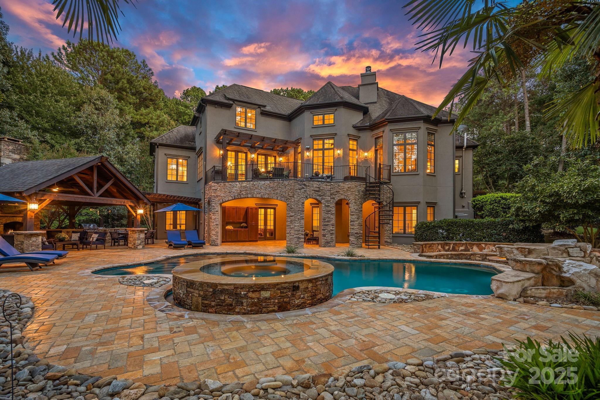 Magnificent 5-bedroom, 5.5-bath waterfront retreat in The Point, showcasing a stucco and stone veneer exterior with a private dock featuring a boat lift and two wave runner ramps, nestled on nearly 2.5 acres of secluded grounds with approximately 425 feet of shoreline. The expansive main level boasts soaring ceilings, modern lighting, and exquisite crown molding throughout. It includes a vaulted-ceiling office, a dining room with wainscoting and tray ceiling, plus a spacious great room with a gas fireplace and coffered ceiling. The kitchen dazzles with brushed gold pendant lighting, honed leathered steel gray countertops, a commercial 48" range, and a generous breakfast area. The primary suite, located on the main level, features a double tray ceiling and a door opening to the patio, accompanied by two guest bedrooms. Upstairs, an additional guest bedroom with a full bath provides extra comfort. The lower level offers a billiard room, family room, gym, two more bedrooms, ample storage, and a lake garage with a workshop. Outside, a luxurious oasis awaits with a heated, saltwater Pebble Tec pool, complete with a waterfall, tanning ledge, and bubblers. The backyard haven features a freestanding covered Travertine pavilion with a tongue-and-groove vaulted ceiling, a wood-burning stone fireplace, a built-in kitchen with Bull Grill, and a portico for al fresco dining. A stone seating area with a gas fire pit completes this breathtaking outdoor retreat.