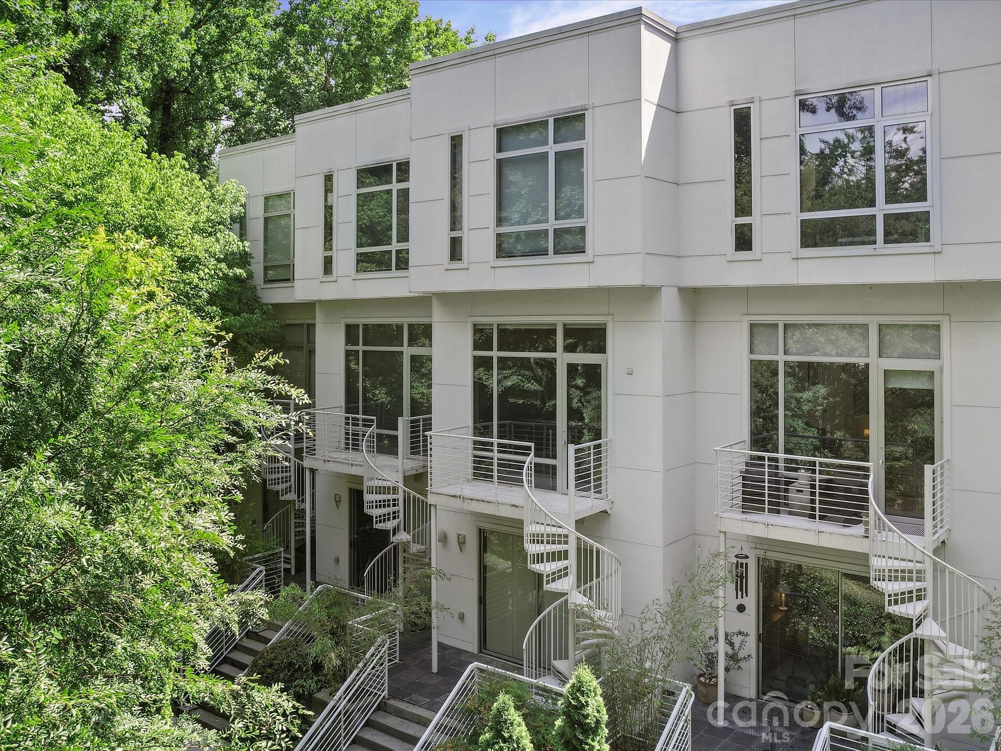 Experience modern urban living in this thoughtfully designed condo in The Celadon, located in the heart of Charlotte's desirable Wesley Heights neighborhood. Enjoy direct access to the Stewart Creek Greenway from your private back patio and a short stroll to Frazier Park, all while being minutes from Uptown Charlotte, Bank of America Stadium, breweries, restaurants, and the upcoming Savona Mill mixed-use redevelopment.
Designed to maximize natural light, this stunning home features floor-to-ceiling windows, a large ceiling skylight, and an open-concept layout with soaring 12-foot ceilings on the main living level.  Immaculately maintained the spacious kitchen is equipped with stainless steel appliances and  gas cooktop that seamlessly connects to the living and dining areas for entertaining. The modern design includes two private balconies—one off the kitchen and another off the living room. A spiral staircase leads from the living room balcony to a second patio, which connects to the Stewart Creek Greenway via a private walking path. The primary suite offers electric shades, a walk-in closet, and a spa-inspired bathroom featuring a deep soaking tub, dual-sink vanity, and contemporary finishes. The ground level provides a versatile flex space complete with a beverage cooler and ice maker, ideal for use as a den, media room, home office, or easily convertible third bedroom. Combining contemporary design, exceptional outdoor access, and one of Charlotte's most walkable locations, this Celadon residence offers a rare opportunity to enjoy the best of city living and nature right outside your door.