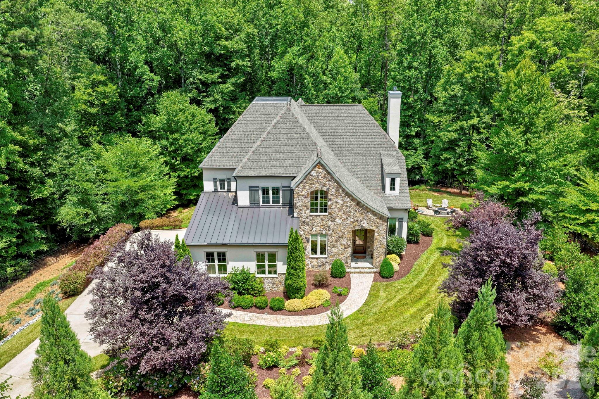 A first offering of this custom-built Simonini home in The Sanctuary, a 1350 acre private community. Lovingly curated and cared for by the original owners, 10530 Sweetleaf Place offers extreme privacy, tucked in the middle of 5 acres and gated. Lush landscaping sets the stage, as you head down the driveway to the remote-controlled gate. The curb appeal is fantastic, with a mixture of stone, hard stucco with metal roofing accents. Inside, a foyer leads to not one, but two dedicated office options. One has built-ins with a window seat. The other, could also serve as formal dining, and has glass pocket doors. There's a drop zone/coat closet/powder room at the rear foyer, an entry from the 3-car garage with wood doors, and room for a workbench. The living room is the heart of this home, anchored by a fireplace, a wet bar, and doors to the four season porch, with its own fireplace, Eze-breeze system for year round use, and stone floor. The kitchen is a cooks dream with a spacious island, walk-in pantry, a Wolf Range, plus wall microwave/additional oven, and a sub-zero built-in refrigerator. It connects to the light-filled dining room with more built-ins, and charming window seat. The primary suite is on the main level, with a coffered tray ceiling, and impressive views to the private backyard. The bath is roomy, with soaking tub, separate vanities with storage, shower with multiple heads, and a customized walk-in closet. Main floor laundry is impressive, with room for a freezer/2nd refrigerator, plus walls of cabinetry and is bathed in morning light. Upstairs, there's a loft, along with three bedroom options, two en-suites. Bedroom four/bonus offers so much flexibility, covering 432 square feet, with custom built-ins and doors to one of two walk-in attic storages. There's also a flex room on floor two, currently used for projects/gift-wrapping. Enjoy dinner al fresco on the back composite deck, or by the stone patio with fire pit in the side yard. This estate is true retreat, where you're close to so much, but feel like you're a world away. Amenity-filled community with more than 20 miles of walking trails, multiple pools, sport courts, playgrounds, and a clubhouse with fitness center situated on the shores of beautiful Lake Wylie. Welcome home!