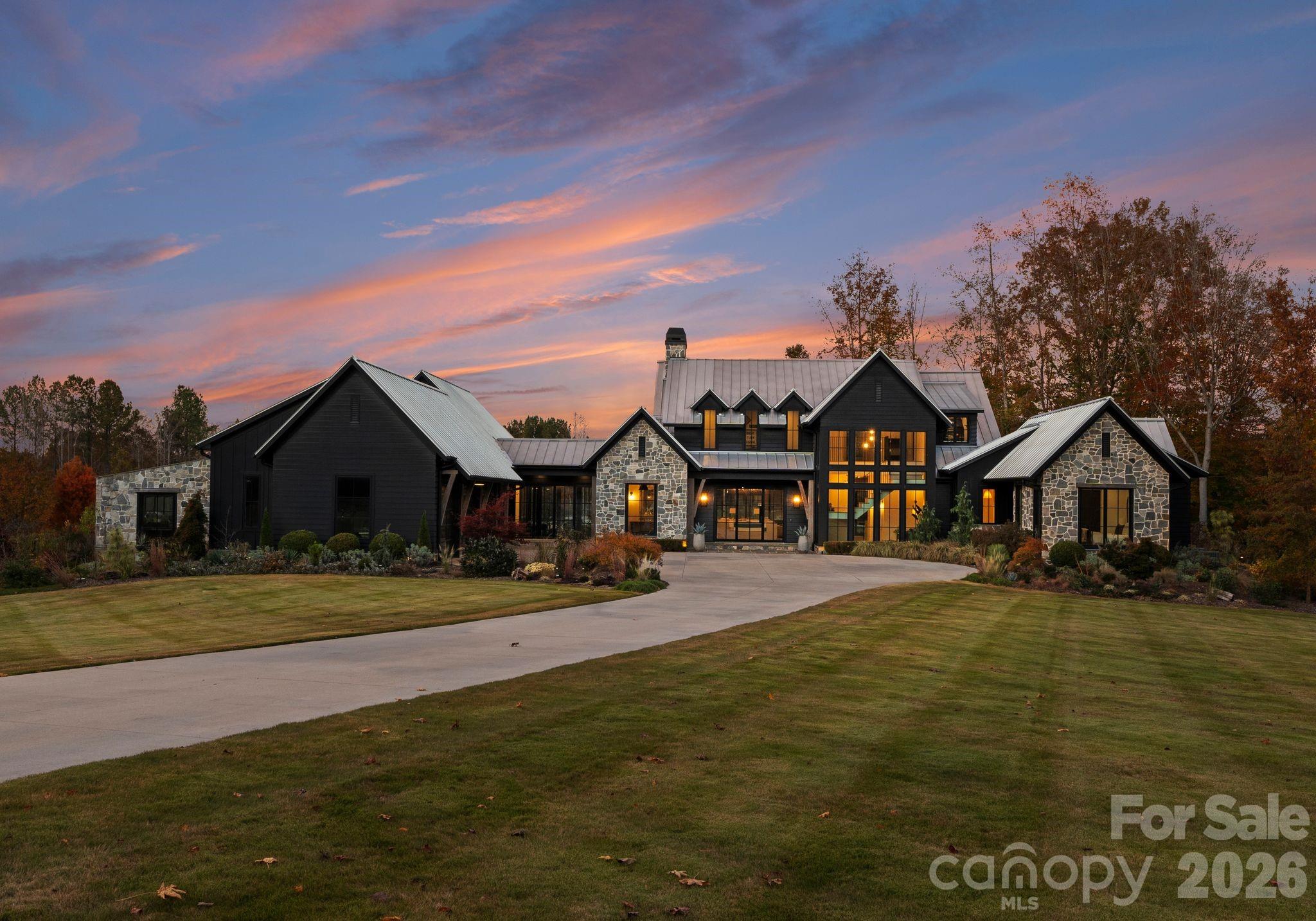 Welcome to Stone Falls Farm-where privacy, design, and lifestyle align on the extraordinary 100 acre modern estate (additional 37-acres available for purchase) just minutes from Lake Norman and Charlotte. Built in 2021, this custom designed residence is set behind a gated entrance with over 1,700 feet of paved drive, offering a rare level of seclusion in Iron Station. Showcasing clean architectural lines, curated finishes, and antique wood beams reclaimed from a 200-year-old Virginia barn, the home blends modern sophistication with timeless character. The main residence offers over 5,400 square feet of living space thoughtfully designed for both everyday living and elevated entertaining. At the heart of the home, the kitchen is both striking and functional, anchored by an expansive island with honed Everest Pearl quartzite countertops and backsplash in the range alcove. A wall of windows fills the space with natural light and seamlessly connects to the surrounding landscape. Thoughtfully appointed with premium appliances including a Wolf gas range, built in Miele espresso system, wine refrigeration, and dedicated beverage fridge strategically designed for function and elevated entertaining. The main level features primary and guest suites, expansive living spaces anchored by dual Isokern fireplaces, a dedicated office or flex room, and seamless flow throughout. Upstairs, two additional bedroom suites, a spacious bonus room, dedicated laundry and a finished walk in storage room providing flexibility for any lifestyle. Outdoor living is equally impressive with a resort-style saltwater pool and spa, flagstone surround, outdoor shower, pool bath, and a covered porch complete with ceiling heater—creating a true year round retreat. A heated greenhouse, whole-home generator, tankless water systems, multi-zone irrigation, and landscape lighting further enhance both comfort and efficiency. Beyond the home, a newly built (2024) 3,000+ square foot conditioned gym and recreation space delivers an unmatched private experience. Outfitted with a commercial FullSwing golf and sports simulator, professional grade fitness equipment, turfed batting cage with pitching machine, wet bar, and custom finishes—including Hemlock accent wall sourced from the Biltmore Estate—this space was designed for both performance and entertainment. Equestrian and lifestyle opportunities continue with a custom barn featuring Barn Pro animal stalls, tack room, loft with future guest suite potential, oversized fire pit, dedicated septic tank, four fenced pastures (two irrigated), along with a chicken coop, covered hay feeders, and thoughtfully designed infrastructure throughout. The land itself is nothing short of remarkable! 100 acres with two flowing year round creeks, abundant wildlife, and miles of trails ideal for horseback riding, ATVs, or simply exploring. Property is currently enrolled in tax deferment program for tax benefits. Despite its privacy, the location remains highly convenient just minutes to a private airport, and within easy reach of Lake Norman, Birkdale Village, Uptown Charlotte, and Charlotte Douglas International Airport. Offered with select personal property including mounted TVs, Sonos system, security cameras and more! This is a fully realized estate offering a rare balance of privacy, scale, and thoughtful design defining the elements of Stone Falls Farm.