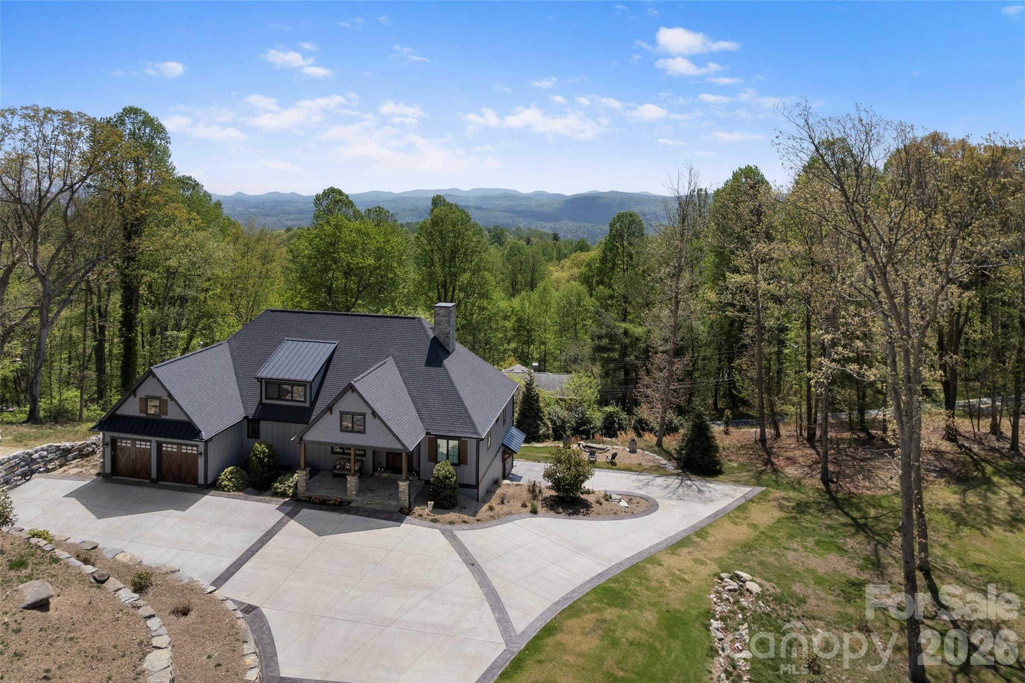 Set on over two private acres with breathtaking year-round mountain views, this custom-built residence in the sought-after Sky Village area of Laurel Park blends luxury, comfort and versatility with two distinct living spaces. From the moment you arrive, a sense of tranquility sets in as this is more than a home, it’s a retreat. Inside, the living room features soaring vaulted ceilings and a striking stone fireplace, creating a warm, inviting atmosphere. The open-concept kitchen is thoughtfully designed with high-end appliances, ample workspace and a generous pantry, ideal for everyday living and entertaining. Expansive Marvin windows frame the surrounding landscape, filling the home with natural light and showcasing the views. A covered porch with its fireplace extends the living space outdoors, offering a setting for year-round enjoyment of the long-range mountain vistas. The terrace level adds flexibility with a spacious recreation room and kitchenette, along with a fully equipped private apartment featuring its kitchen and laundry. Additional highlights include a two-car garage and whole-house generator. Just minutes from Jump Off Rock and downtown Hendersonville, this property offers peaceful mountain living with convenient access to modern amenities.