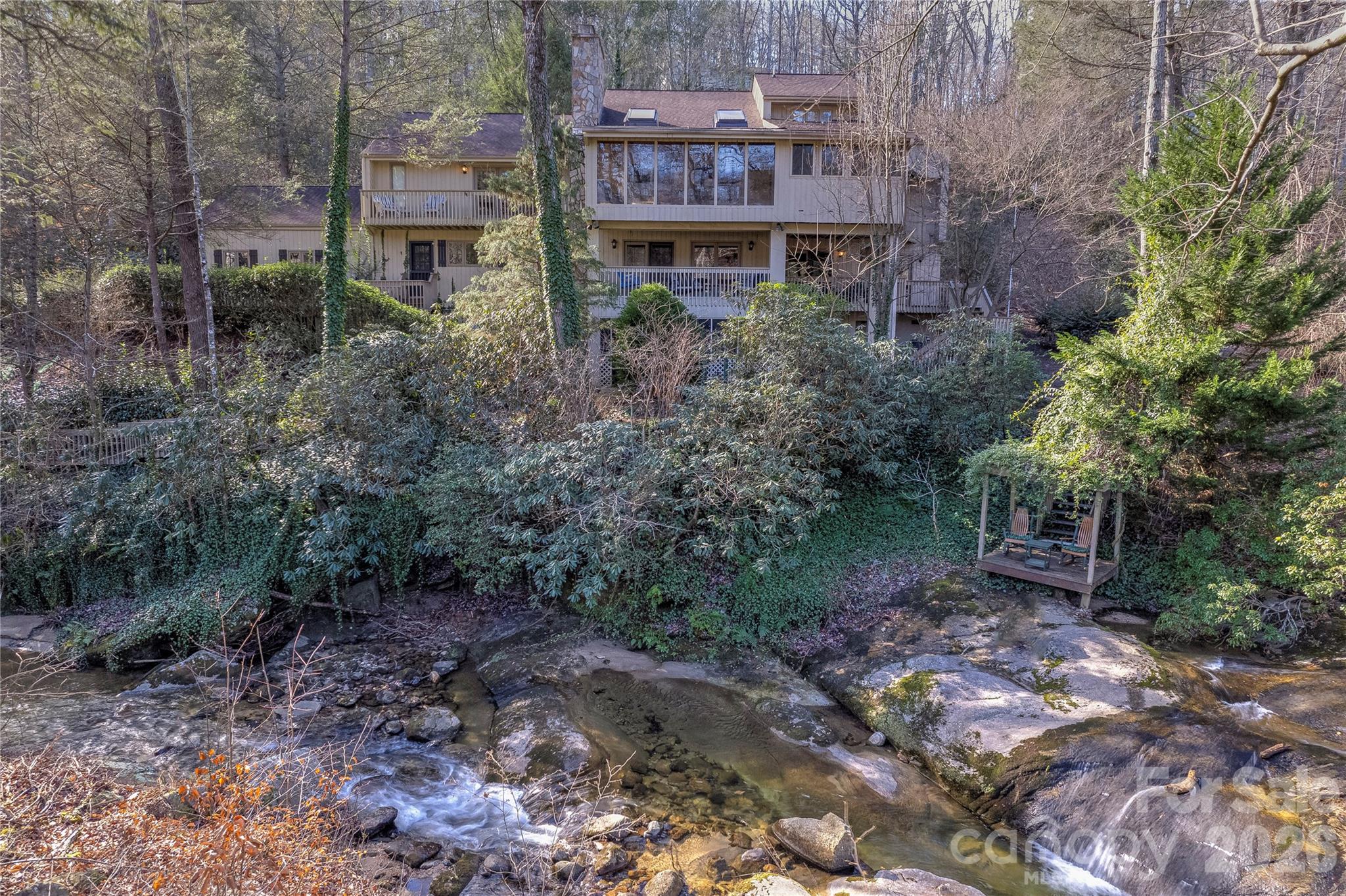 Tucked within the gates of Rumbling Bald, this private mountain retreat offers the rare combination of walkability to amenities and a breathtaking natural setting. Set on 1.66 acres, the home overlooks the gentle flow of Buffalo Creek, complete with your own cascading waterfalls, creating a truly serene, park-like backdrop. Thoughtfully designed across four expansive levels, this residence effortlessly accommodates both everyday living and hosting extended family or guests. Three spacious decks invite you to take in the sights and sounds of the creek, offering the perfect setting for morning coffee or evening relaxation. The main level features a tranquil primary suite with a cozy wood-burning fireplace, an updated bath, and generous walk-in closet. The heart of the home is a large, well-appointed kitchen that opens to a sunroom, ideal for soaking in the surrounding beauty, alongside an inviting living area with a gas fireplace. Upstairs, a charming sitting area provides a quiet retreat for work or reading. The second level offers two bedrooms with direct deck access, a spacious living room with gas fireplace, and a versatile oversized laundry/game room conveniently connected to the two-car garage. The ground level is designed for entertaining, featuring a screened porch with winding paths leading to Buffalo Creek, a generous living area with a third gas fireplace, a built-in bar, and an additional flex room, perfect for guests or rental flexibility. With its exceptional layout, stunning natural surroundings, and access to all the amenities of Rumbling Bald, this property is ideally suited as a full-time residence or multi-family income producing vacation rental.