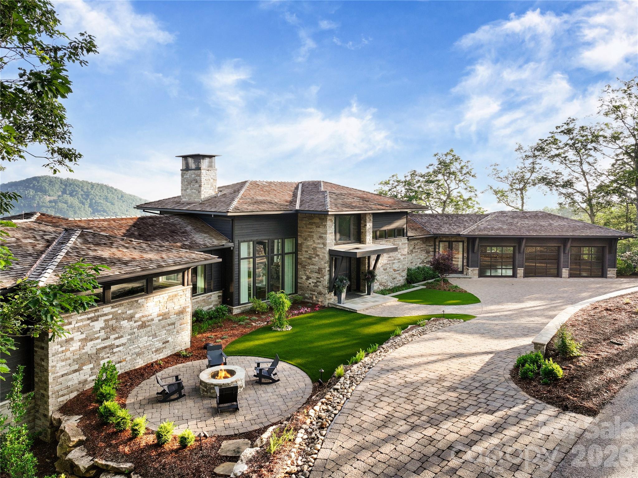 Soaring above the Blue Ridge Mountains in The Cliffs at Walnut Cove,  Asheville’s only private gated golf community, 510 Cloud Top Way delivers year-round, long-range mountain views from virtually every room in the house. Completed in 2023 and crafted by Dillard-Jones Builders, a Preferred Builder with The Cliffs and interiors by Tribus Interior Design, this 7,400+ square-foot residence on 1.07 manicured acres is as technically sophisticated as it is visually striking. The stacked stone and cedar exterior, cedar-shake roof, and blue flagstone entry set a tone of grounded, intentional luxury — then the steel entry door opens, and the scale of the two-story great room, exposed steel beams, and a wall of expansive mountain views take over. The main level is designed for the way people actually live. A kitchen outfitted with Wolf and Sub-Zero appliances anchors the open floor plan, featuring an 11' x 5' island, solid quartz backsplash, and a concealed pantry stocked with a second Sub-Zero refrigerator and wine cooler. The dining and great room flow seamlessly to a fully outfitted outdoor deck with a built-in Sedona gas grill, retractable phantom screens, and IPE decking — an extension of the home living space, with protected views of Pisgah National Forest and sweeping sightlines to downtown Asheville and the Biltmore Estate. Two dedicated home offices — one with custom-soundproofed walls — meet the demands of modern professional life without sacrificing the view. The primary suite is a masterclass in quiet luxury: coffered ceilings, French doors to the private deck, and a custom floating king bed. The  spa bathroom continues the standard with radiant heated marble floors, a zero-entry steam shower with treetop views, a Bain Ultra soaking tub, and a marble wardrobe island anchoring the expansive primary closet. The lower level fully expands the home's personality. A beamed media room with a MadVR Envy video processor and wall screen anchors the space, with a bar kitchenette with a Marvel keg refrigerator, waterfall quartz island, and glass-front Sub-Zero, and a temperature-controlled glass wine cellar steps away. On one end, a dedicated gym with epoxy concrete floors and separate HVAC, and a guest suite with en suite bath. On the other end, another primary guest suite with en suite bath, a bunk suite sleeping four, and an additional guest suite — space for family, guests, or full-time multigenerational living, all with the same long-range views. Infrastructure is equally uncompromising: a 48KW Kohler whole-house generator, Savant smart lighting and sound, three-zone Lennox HVAC, three Navien on-demand water systems, FloLogic leak detection, Ultravation air filtration, EV charger, home elevator, and a Savant-integrated exterior sound system including a firepit with hidden speakers. Where the mountains meet masterful design, 510 Cloud Top Way stands in a category of its own. A club membership at The Cliffs is available for purchase with this property giving you access to all seven communities.
