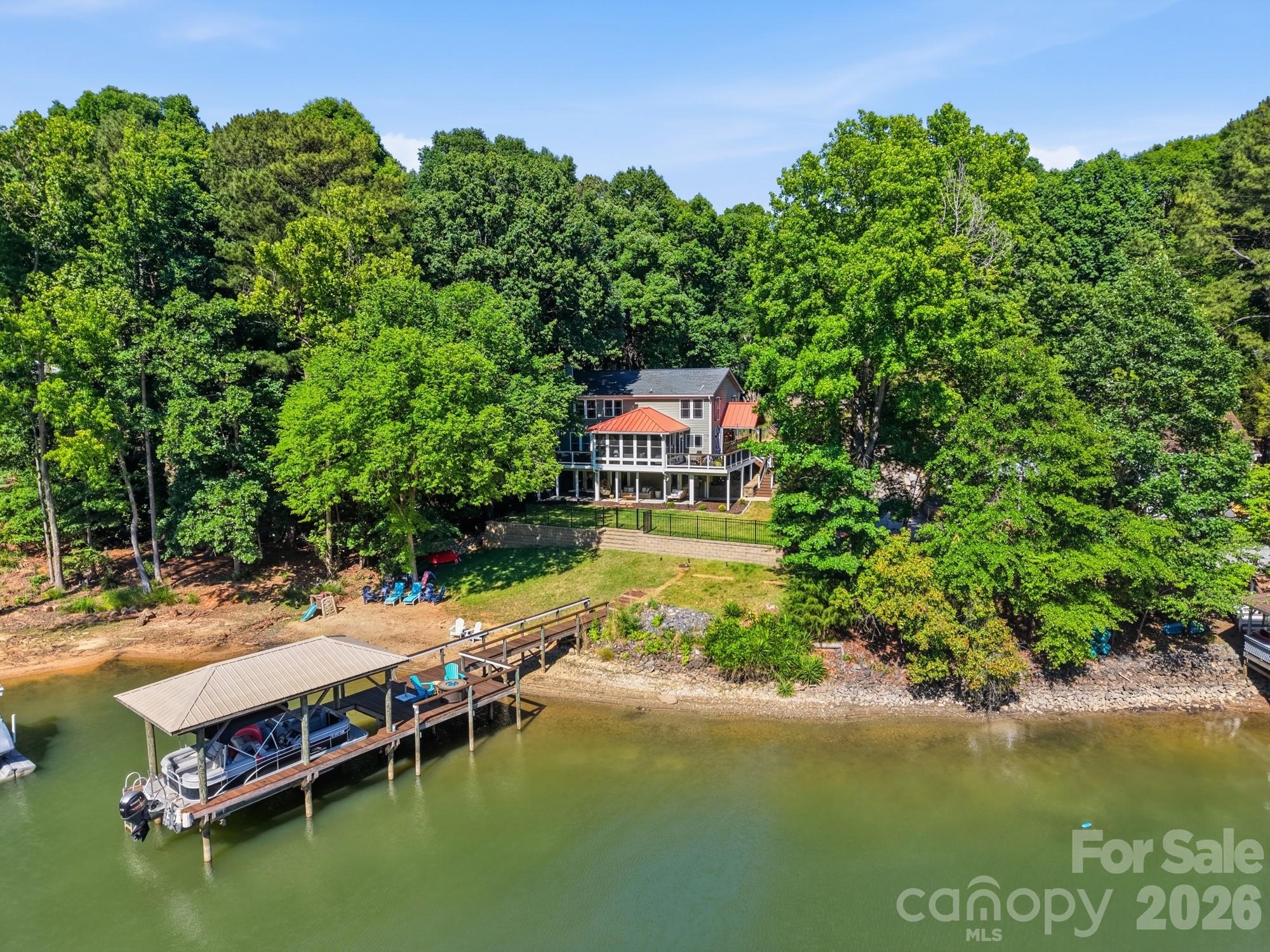Rarely does a waterfront home in Tega Cay offer the perfect blend of move-in-ready luxury and lasting privacy. This fully updated retreat features a flat, fenced backyard that gently slopes to a covered deep-water dock, large sandy beach, and swimming area, all framed by peaceful lake views and the added seclusion of a non-buildable wooded neighboring lot. Inside, the open-concept chef’s kitchen is truly a showpiece with a 48” double oven range, two 27” Sub-Zero refrigerated drawers, built-in professional refrigeration, and a massive granite island with seating for eight. Floor-to-ceiling lake views pour into the year-round sunporch and nearly every room in the home. The upper level offers a spacious primary suite along with three additional bedrooms, while the walk-out lower level features a beautifully tiled in-law ensuite complete with its own bedroom, bath, and kitchen. High-end finishes include teak hardwood floors, fresh paint, new carpet, custom soft-close cabinetry, and a striking stone-surround fireplace. Major upgrades such as new air conditioning, replacement windows, cement board siding, and a standing seam metal roof over the two-car porte cochere add both style and peace of mind. Outdoor living is equally impressive with professional grading, Trex decking, and a covered paved patio featuring recessed lighting and fans. Tucked away at the end of a quiet cul-de-sac, this turnkey waterfront property offers exceptional privacy while remaining convenient to everything Lake Wylie has to offer — the perfect setting for relaxing, entertaining, and enjoying unforgettable lakefront living year-round.