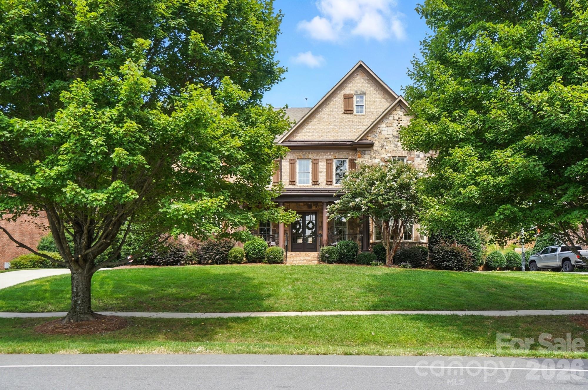 This exceptional residence blends timeless elegance with thoughtful design, beginning with an expansive rocking chair front porch that welcomes you into a dramatic two-story foyer highlighted by a sweeping circular staircase. The main level is beautifully appointed with formal living and dining spaces, a sunlit great room with a gas fireplace, an oversized chef-inspired kitchen, and a private guest suite with ensuite bath.

Upstairs, you’ll find three generously sized secondary bedrooms, a spacious bonus room, an oversized laundry room with utility sink, and a remarkable primary retreat designed for comfort and sophistication. The spa-inspired primary bath features dual private sides, each with its own vanity, sink, water closet, and walk-in closet, seamlessly connected by an expansive designer-tiled shower.

The third level offers an impressive private living space ideal for extended stays, entertaining, or flexible lifestyle needs. Complete with a second full kitchen, dedicated laundry room, living area, office, and a bedroom featuring beautiful windows overlooking the serene, tree-lined backyard, this level also includes a spacious walk-in closet.

Situated on a beautifully landscaped homesite in the highly sought-after Olmsted community, the outdoor living spaces are equally captivating. The tiered backyard includes a large flat recreation area, a stunning stone patio, and a wood-burning fireplace perfect for year-round enjoyment. An extended driveway provides additional parking convenience.

Residents of Olmsted enjoy exceptional community amenities, including resort-style pool and recreation areas, tennis courts, and a picturesque lake ideal for peaceful afternoon to relax and take in nature. Be sure to request the complete list of upgrades and community details from your agent. This is a rare opportunity to own a truly remarkable home.