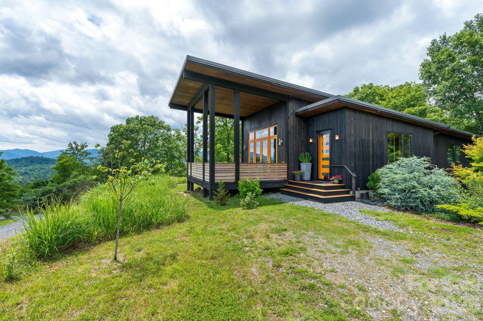 Inspired by the Blue Ridge Mountains, this stunning architect-designed, award-winning, magazine-featured, green-built, massive mountain-view home and separate studio settle comfortably and serenely into 18 acres of lush gardens and trees offering relaxation, recreation, and inspiration. Luxury abounds on this private property--from the walls of windows framing views at every turn, to curated finishes, to beautifully appointed built-ins--each room of the home offers its own experience and "wow" moments! The thoughtful and efficient design allows large gatherings in the great room to spill out to the deck and gardens under the stars while still preserving privacy for the inhabitants in the tucked-away bedrooms, office nooks, and bathrooms. Clever touches such as the main bathroom that converts to a half bath with the slide of a glass pocket door, invisible solar panels, and whole house air filtration system (ERV) offer so much versatility and attention to detail. The lower level presents yet another private living space with a separate exterior entrance (and interior entrance) and has its own efficiency kitchen, bedroom/living space, full bath, and a large, lovely patio with mountain views. From the main home, it's a short stroll past the rose bushes and across the drive to the art and music studio. This bright and calm space is so versatile! Currently used as a drum studio on one side and an art studio on the other with a loft in-between, this building could easily be converted to another full living space. It even has its own patio and giant sliding glass doors! If music and art are your thing, you will be delighted with the soundproofing in the drum room and Northlux full-color spectrum lighting in the art studio. So much to inspire here! The land offers privacy among the professionally-tended wildflower gardens that surround multiple grand-view building sites graced by uplifting sunrises and nurturing sunsets! The location is so convenient, too. You'll feel worlds away from it all while only being five minutes to Main Street Marshall and its festivities, cafes, restaurants, and art studios and only 22 minutes to downtown Asheville!