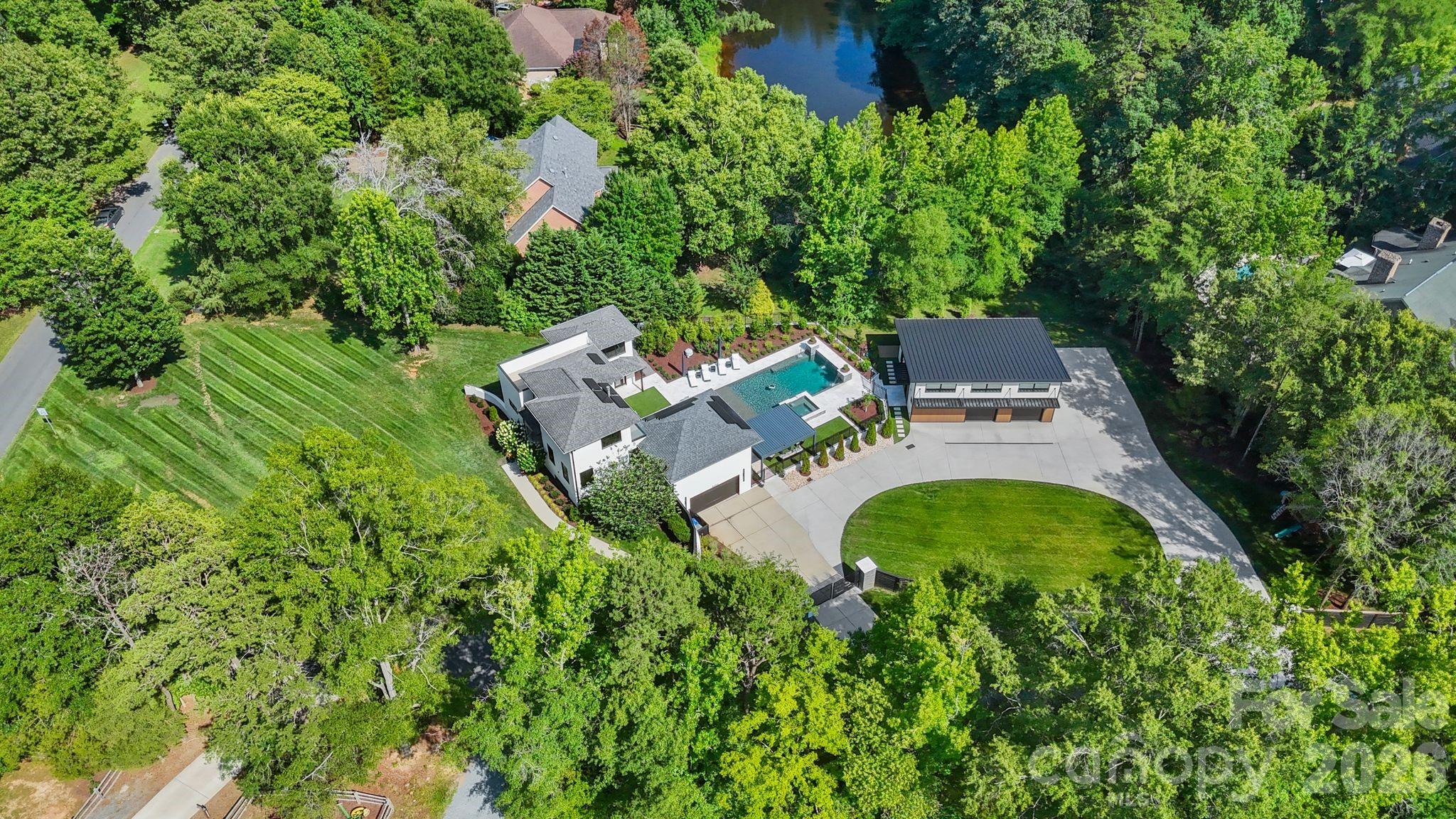 Modern architecture, private acreage, and resort amenities rarely converge in the Weddington school zone, and 1064 Greylyn Drive delivers all three. Set on 1.58 acres on a quiet cul-de-sac, this contemporary estate offers more than 5,500 square feet under roof, including 4,125 sq ft of heated living area across the main residence and accessory building, 4 bedrooms, 5 full baths, multiple bonus and flex rooms, a resort-style pool, and 4-car garage capacity across two garages. Zoned for top-ranked Antioch Elementary, Weddington Middle, and Weddington High, with quick access to I-485.

Since 2022, the property has been transformed through a comprehensive owner investment of exceptional scale and quality, reimagining the home and grounds with a full designer kitchen, the pool and outdoor living environment, the accessory building, and whole-property systems. The result is a 2015-built home that lives like new construction.

An oversized black steel pivot door announces the home's design intent from the first step inside, opening to a main level where the brand-new kitchen showcases custom walnut cabinetry, a dramatic waterfall quartz island with matching quartz backsplash, and a new suite of stainless ZLINE appliances. Rich Brazilian walnut hardwoods flow throughout the entire main floor, anchored by a sculptural spiral staircase refinished in matching Brazilian walnut, a warm counterpoint to the home's crisp modern lines.

The residence pairs clean contemporary architecture with serious infrastructure: rooftop solar, Tesla charging, security cameras, dual-zone heating and cooling, and a private-entrance suite ideal for in-laws or guests. Three levels of living include a rooftop terrace, loft, and generous flex spaces that adapt to home offices, media, gym, or hobby rooms. An oversized, fully gated circular drive delivers abundant guest parking and four garage bays, with the attached two-car garage joined by two more in the accessory building, and dual LiftMaster smart gates providing secure, WiFi-controlled access.

The backyard lives like a private resort. A 20x40 heated pool with 8x8 spa features sheer-descent waterfalls, benches, and a tanning ledge, surrounded by marble hardscape decking, low-maintenance turf, landscape lighting, and a smart louvered pergola, fully fenced with rear irrigation.

The showpiece accessory building adds 444 sq ft of finished living with a kitchenette, full bath, laundry, and conditioned loft, alongside an 880 sq ft fully conditioned oversized double garage featuring radiant in-slab heated floors with polyaspartic coating, wiring for a car lift and EV charging, a plumbed pressure washer, hot and cold exterior faucets, hardwired fiber internet, and a deck overlooking the pond. Guest quarters, studio, or the collector's dream garage.

Private acreage, modern design, and turnkey systems rarely found together in the Weddington school corridor.