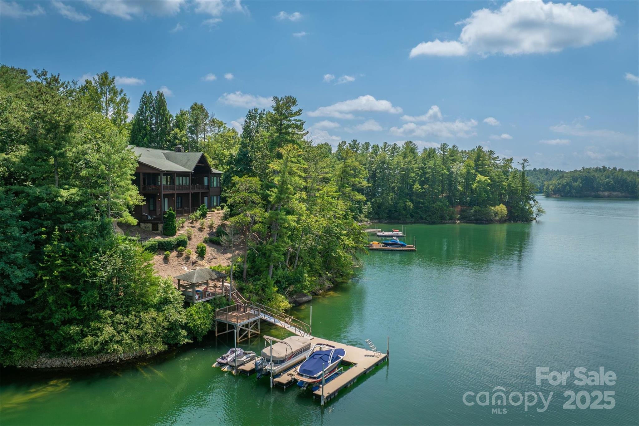 Discover a world where the majestic Blue Ridge Mountains and the tranquil waters of Lake James become your daily backdrop. This stunning 6,000+ sq ft home offers an unparalleled living experience, a perfect blend of natural beauty and refined luxury. The heart of the home is the great room, where a floor-to-ceiling stone fireplace provides a rustic & elegant focal point and massive windows flood the space with light and frame breathtaking, panoramic views of the mountains and lake. Rich hardwood floors extend throughout the home, connecting each space with timeless style. Designed for both relaxation and entertaining, the home features five full bedrooms plus additional sleeping quarters, including a pocket bunk room and a additional room over the garage made for all your guests. The primary suite on the main level also has long range views and a spa-like en-suite bath with a soaking tub and a large walk-in shower. The gourmet kitchen is a chef's dream with island seating, Sub zero refrigerator, gas cooktop, warming drawers, beverage refrigerator and complete with a walk in pantry.  Step outside onto the upper and lower patios to savor the stunning vistas and amazing sunsets. A gently sloping path leads to a covered gazebo and private two-slip steel reinforced dock, resistant to the worst wind and wake surfing craft.  This is more than a home; it’s truly the Lake James lifestyle. Sold furnished providing a complete turnkey opportunity. Southpointe has community pool, Dry Creek walking trails and direct access to the Fonta Flora Trail. Just 15 minutes to downtown Morganton for shops & entertainment.