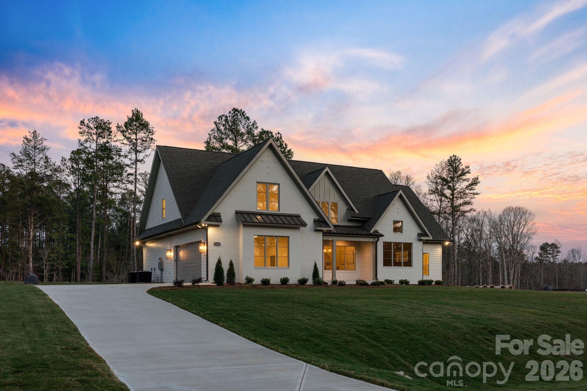 Nestled within an intimate 36-homesite community where every residence sits on over an acre of land, this exceptional home represents a level of craftsmanship and architectural detail rarely found in the Clover market. Perfectly positioned along the community pond, the property enjoys peaceful water views and a setting that blends privacy, space, and natural beauty.

From the moment you arrive, the striking exterior architecture and beautifully manicured grounds set the tone for what lies inside. Full sod and irrigation frame the home, while the thoughtfully designed layout and placement on the homesite create an inviting sense of openness and tranquility.

Step inside and immediately appreciate the refined design and attention to detail. Elegant architectural arches create graceful transitions throughout the home, adding a level of character and sophistication rarely seen in newer construction. The open floor plan allows natural light to fill the main living spaces, while a carefully curated lighting package enhances the warm and welcoming atmosphere.

At the heart of the home is a stunning chef’s kitchen that balances beauty and functionality. Extensive custom cabinetry, a statement vent hood, marble countertops, farmhouse sink, and high-end appliances create a space designed for both entertaining and everyday living. The kitchen flows seamlessly into the spacious living area, where a sleek fireplace and thoughtfully designed built-ins create the perfect setting for gathering with family and friends.

The primary suite offers a peaceful retreat, featuring a beautifully designed bath complete with a large walk-in shower, freestanding soaking tub, and custom cabinetry that blends elegance with everyday comfort.

Upstairs, additional bedrooms and well-appointed bathrooms provide comfortable accommodations for family and guests, while a spacious upper-level bonus area offers flexibility for a media room, playroom, home office, or secondary living space.

Outdoor living is equally inviting. The covered rear patio overlooks the community pond, creating a serene backdrop for morning coffee, evening relaxation, or entertaining while enjoying the quiet natural surroundings.

Located just minutes from dining, shopping, coffee shops, and everyday conveniences — and only a short drive to Charlotte Douglas International Airport — this remarkable property offers the rare opportunity to enjoy space, privacy, and luxury living in one of Clover’s most distinctive communities.

This is more than a home — it is a showcase of quality, thoughtful design, and timeless craftsmanship.