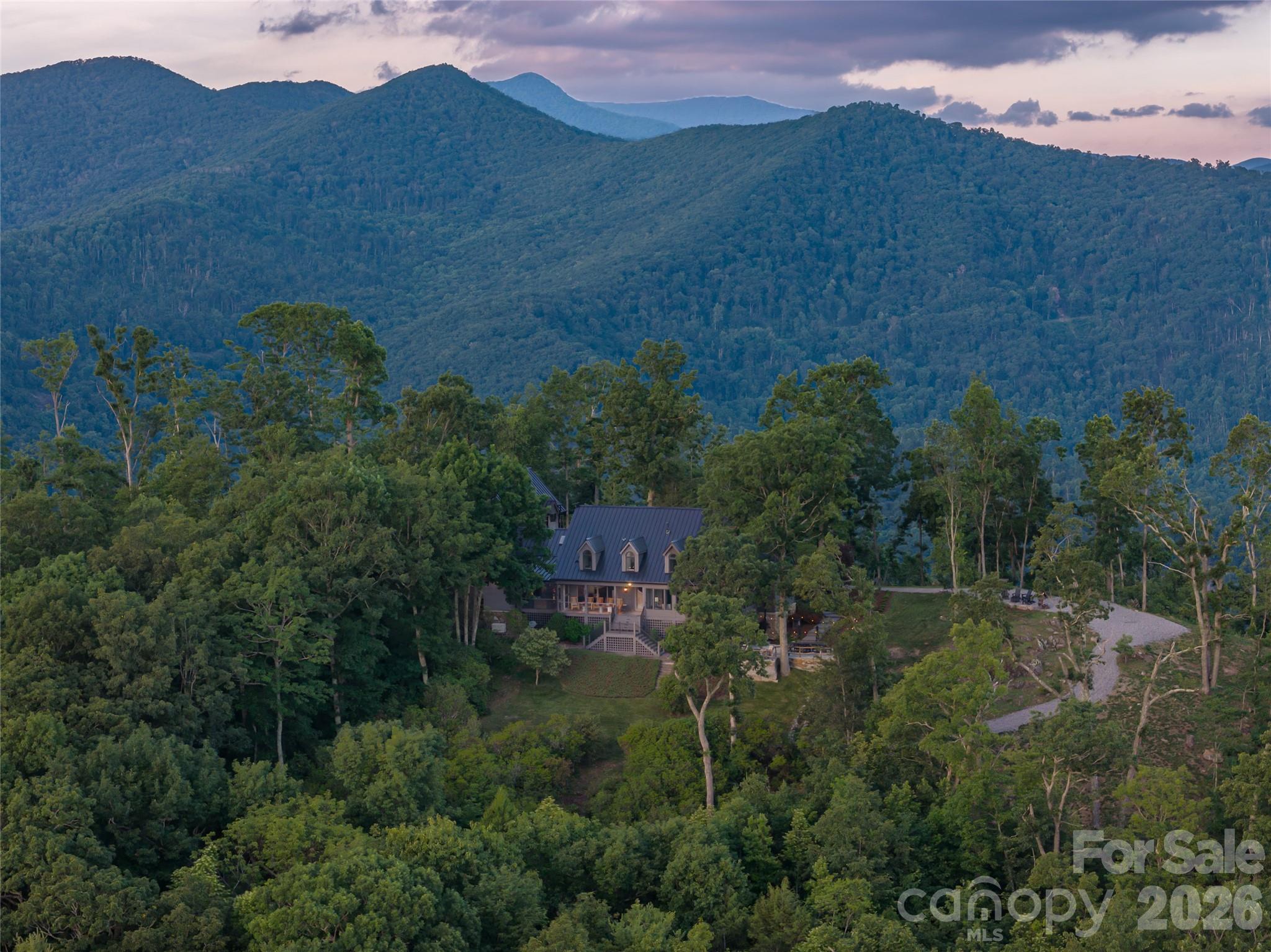 Commanding an extraordinary mountaintop setting just off the Blue Ridge Parkway, this exceptional custom estate is a rare expression of refined mountain living. Set on approximately six private acres, the property captures breathtaking panoramic views that stretch for miles, creating an unforgettable backdrop in every season. Thoughtfully designed outdoor living spaces—including multiple seating areas and fire pits—invite quiet mornings, unforgettable sunsets, and effortless entertaining surrounded by the beauty of the mountains.

Natural light pours through expansive windows, beginning in the welcoming entry foyer that doubles as a sun-filled sitting room. Beyond, soaring vaulted ceilings define the dramatic great room, where an open balcony above and walls of glass create an impressive sense of space while keeping the extraordinary views at the forefront.

Designed for both everyday living and exceptional entertaining, the chef's kitchen is appointed with premium Wolf appliances, a commercial-grade salamander, steam oven, and an impeccably equipped butler's pantry. Just beyond, an intimate viewing room offers one of the home's most captivating spaces, where every window frames the surrounding mountain landscape.

The main-level primary suite provides a peaceful retreat with custom barn-door closets and tranquil views. Upstairs, two spacious guest suites, two full baths, and a versatile bonus room offer exceptional accommodations, while a richly appointed office provides an inspiring workspace. The lower level features a generous recreation room and half bath.

The estate also includes an attached two-car garage, as well as a separate three-car garage connected by a covered walkway. Above, a beautifully finished private apartment with its own bedroom, bath, living room, and kitchen offers ideal accommodations for guests, extended family, or a caretaker.

A home of remarkable craftsmanship and enduring elegance, this is a place where architecture and landscape exist in perfect harmony—offering extraordinary privacy, exceptional amenities, and one of the area's most spectacular mountain settings ready for you to call it home.