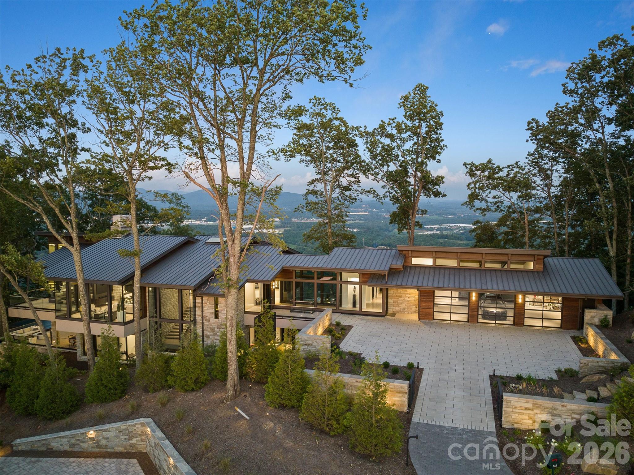 A Showcase Mountain Estate with Panoramic Views in Western North Carolina’s Blue Ridge Mountains.

Located at 2,840 feet along a ridgeline in The Cliffs at Walnut Cove, 515 Cloud Top Way is a contemporary mountain residence offering long-range views, privacy, and architectural prowess just minutes from downtown Asheville. Situated in Arden, North Carolina, the home overlooks the Blue Ridge Mountains of Western North Carolina and offer for north-, east-, and south-facing views.

The masterpiece residence offers 7,362 square feet of indoor space across two levels, was designed by Young and Young Architects and custom built by Glenwood Custom Builders. The architecture emphasizes clean horizontal lines, massive windows, and inspirational use of stone, wood, glass and other natural elements.

Featured in Carolina Home + Garden (Winter 2023), the property sits on 2.46 acres adjoining protected national forest land, ensuring long-term privacy and preserved views.

Interior spaces are defined by floor-to-ceiling glass, natural wood, steel, stone, and backlit quartzite. The main living level includes a great room, a chef’s kitchen with Sub-Zero and Wolf appliances, illuminated quartzite backsplash, and a fully equipped back kitchen designed for entertaining.

Additional spaces include a dedicated bar room and a professional-grade fitness center with Cybex, Hammer Strength, and Precor equipment. A three-car garage includes an integrated EV charging station.

The six-bedroom layout provides separation and privacy, with most bedrooms offering ensuite baths and mountain views. Outdoor living centers on an infinity-edge pool and spa positioned at the edge of the landscape, complemented by a cabana with a large outdoor television and motorized retractable screens.

The home features integrated systems including Lutron lighting and shade control, Sonos whole-home audio, Tesla Powerwall with solar panels, a Generac generator, and a comprehensive camera security system.  Heating system is Geothermal, with six zones of heating and cooling.

Residents of The Cliffs at Walnut Cove have access to a Jack Nicklaus Signature Golf Course, clubhouse, wellness facilities, fine dining, tennis, and hiking trails. A Cliffs Club membership is available by separate application. In September 2026, the community will host the inaugural Biltmore Championship Asheville, marking the return of the PGA Tour to the region.

Convenient to downtown Asheville, Asheville Regional Airport, and the Blue Ridge Parkway, 515 Cloud Top Way represents a modern mountain home defined by architecture, setting, and location.