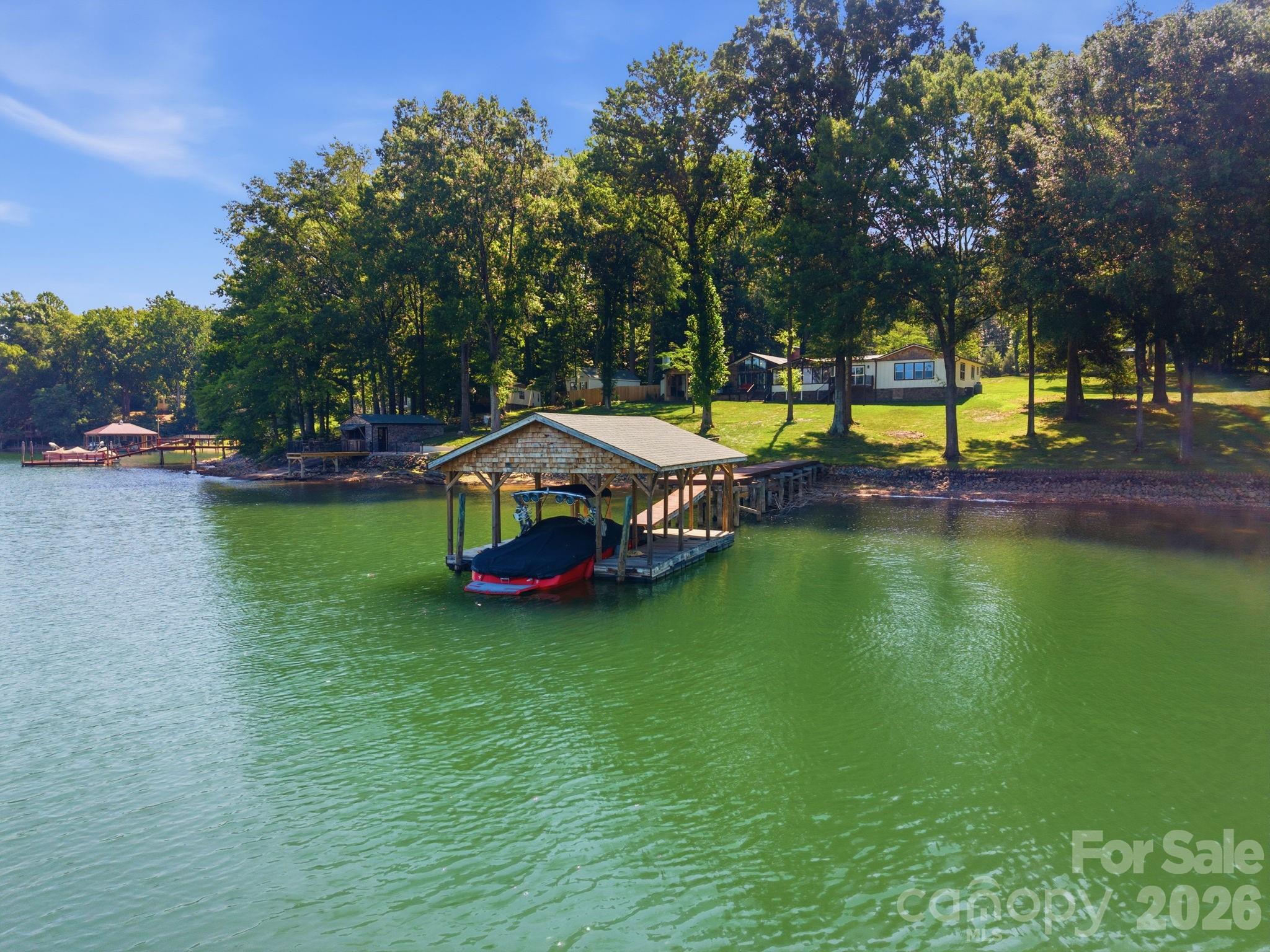 Rare Lakeside Perfection on Lake Norman! Welcome to this masterfully updated and expanded sprawling ranch, perfectly positioned on a premier, flat 1.19-acre waterfront lot. Blending modern farmhouse elegance with cozy rustic charm, the home’s exterior commands attention with its striking architectural mix of natural stone, classic board-and-batten siding, warm cedar shake accents, a durable metal roof and attached carport. Offering ultimate privacy and nearly 200 feet of shoreline on a pristine deep-water cove, this estate delivers the most coveted, hard-to-find lake amenities—including your own private boat ramp and a finished boat house complete with a bar and A/C! Inside, the home radiates custom character and architectural warmth. The entry foyer opens to a jaw-dropping, open-concept kitchen and dining pavilion, bathed in natural light beneath vaulted knotty-pine ceilings with exposed beams. This culinary haven boasts premium stone counters, a shiplap backsplash, two-tone cabinetry, and a massive deep-blue island with a butcher block top. High-end stainless appliances (including a double oven and KitchenAid fridge) make hosting effortless, while a magnificent, floor-to-ceiling natural stone fireplace anchors the room. Just beyond, a generous casual dining space features a fully equipped wet bar/beverage station with a wine cooler, prep sink and rustic open shelving. A cabinet door conceals incredible walk-in pantry storage. Designed for seamless single-level living, the floor plan flows beautifully into multiple lakeside living spaces, including a cozy living room complete with a classic wood-burning stove for chilly lake nights. Enjoy a formal dining experience in the sunroom surrounded by floor-to-ceiling windows framing wide-water views. Tucked away for maximum privacy is the spectacular, newly added primary retreat. This luxurious sanctuary features a private office, massive walk-in closet and a spa-like en-suite with a double vanity, soaking tub and custom walk-in shower. Three additional bedrooms—each rich with unique character and custom wood finishes—are flanked by two beautifully updated bathrooms. A convenient lakeside bonus room with laundry and sink serves as the perfect transition after a day on the water. The outdoor oasis is second to none. Entertain across multiple lakeside venues, including a newly completed covered porch with an outdoor fireplace, a dedicated fire pit area, a private deck off the owner's suite, and the ultimate air-conditioned boat house bar. A rare blend of privacy, flat acreage with room for a pool and deep open water—this Lake Norman retreat is truly irreplaceable!
