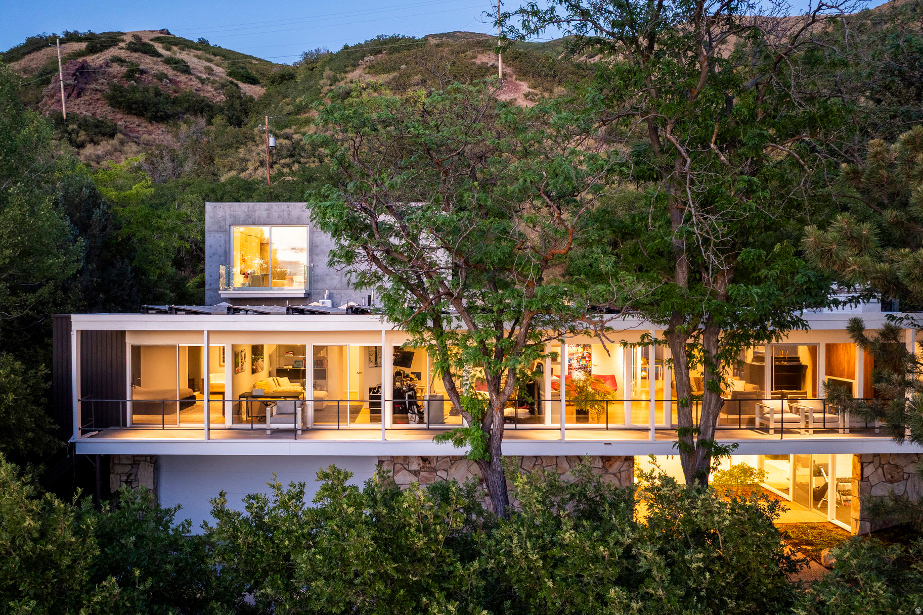 On one of Salt Lake's most sought after streets, this extraordinary home is a masterclass in architecture, proportion, and design. Set back from the street and intentionally private, the property carries a quiet confidence. The approach is centered on symmetry and balance. A broad walkway leads to the double entry doors, while floor to ceiling glass spans the full length of the upper level. Above the stone walls below, a cantilevered veranda reinforces the home's strong horizontal lines. Inside, a gallery style hallway runs through the core of the home, terminating at a fully framed north facing wall of glass that draws the landscape directly into view. Originally designed by renowned architect Jim Christopher, the home already possessed remarkable architectural integrity. A meticulous renovation elevated the original structure while preserving its intent. The property was further expanded by Sparano + Mooney with a striking modern addition known as The Cube, completed in 2025 as part of the home's transformation. The Cube is a bold composition of glass and concrete that complements the original home. In 2025, it received one of only five residential design awards presented nationwide by the American Institute of Architects. Reflections from the pool move across the glass facade, while polished concrete floors, exposed concrete walls, floating stairs, and a dramatic Poliform library wall define the space. The architectural language extends throughout the outdoor spaces, including the pool, garden, and hot tub, which sits just above the roofline behind a concrete privacy wall to capture sweeping sunset and city views. From the herringbone floors and vintage hardware to the Italian cabinetry, every detail was carefully considered. This is a rare opportunity to own a home where original architecture, thoughtful renovation, and nationally recognized contemporary design come together in exceptional harmony.