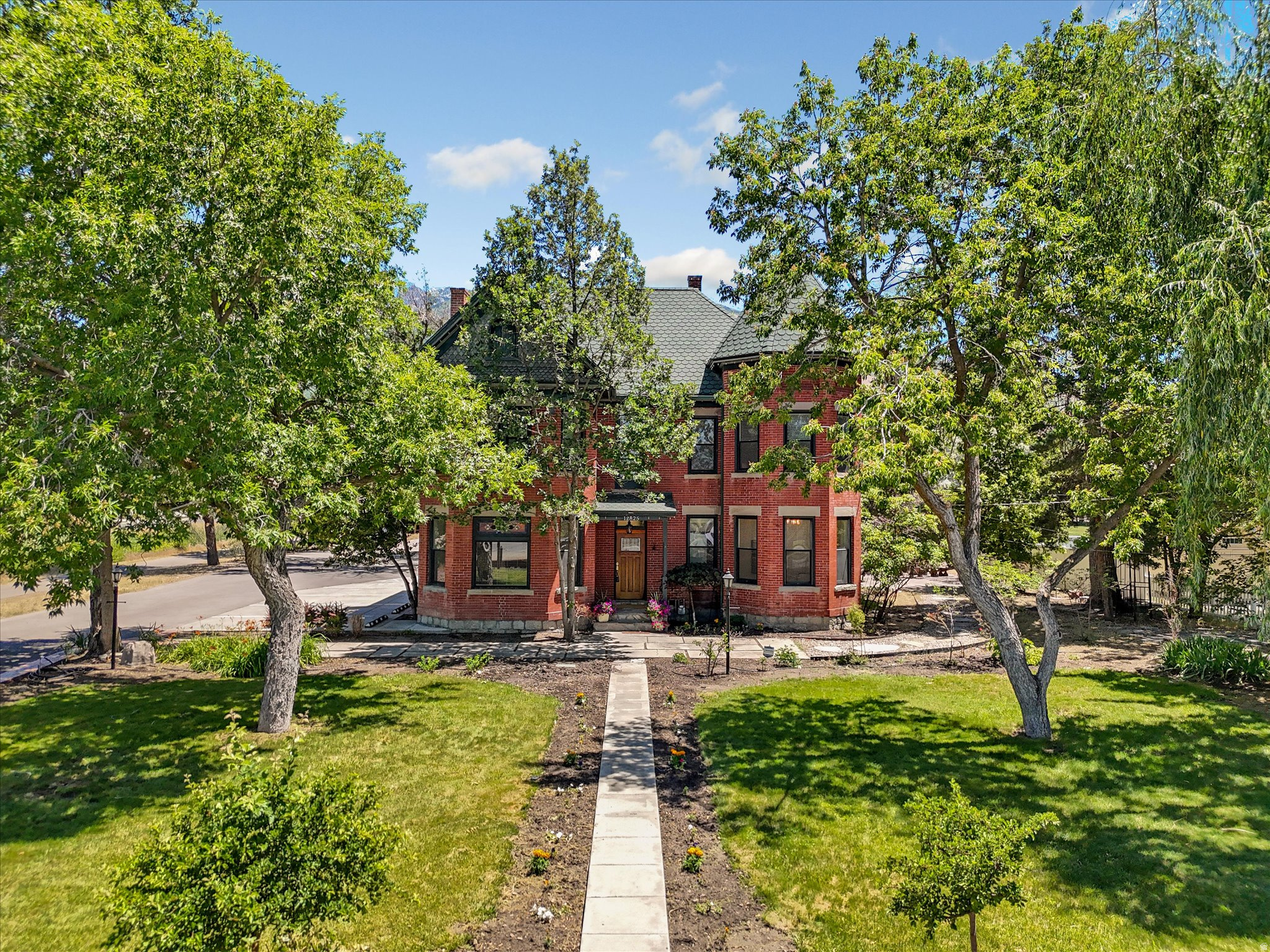 *Open House Sat. July 18th 10am-1PM* How do you even describe a home as special as this one? The Joseph S. Nielsen Home on Fort Street is a two-and-a-half story red brick Queen Ann with a granite foundation that sits on nearly an acre in Draper, Utah. But the legacy goes so much deeper. Built for Joseph, a school teacher and farmer, and his wife May, a musician; this home has been a happy place for families and friends for over a century. Over the years it has evolved from a family homestead with an orchard and vegetable garden, to divided apartments, to a full and glorious restoration to a historic mansion, and then its most recent transformation to Chestnut Pines where it was the only cafe in the United States to serve dishes exclusively from sprouted ancient grains. That brings our story to present day where this singular landmark property is ready for its next chapter where you become the next steward of our story. There's no obligation to follow a script; if the past has taught us anything it's that this timeless home can adapt through the ages. The bones are original. That granite foundation is solid and holds 2.5 stories of red brick, a grand staircase, tall ceilings and original wood floors. Exposed brick is spotted throughout, accented by period-style doors and hardware along with bay windows that flood the front rooms with natural light. The craftsmanship connects with you a time when we built things to last, and makes you appreciate the past. Extra care has been given to keep the original character while also fully updating all electrical, plumbing, and HVAC and bringing the home into ADA compliance. The kitchen is built for people who take food seriously; this was a farm and homestead, after all. That heritage is honored with modern updates like a butler's pantry with additional counter space, a beverage kegerator, two sinks, a mini freezer and fridge, and room to really make use of the fresh whole foods you could grow here. Behind the main home there is a renovated cottage that houses a fully equipped commercial kitchen. Whether you continue a food-focused operation, lease it out, or keep it for your own hobby kitchen, it's ready now. You can still feel Joseph and May's vision come to life in the landscape. They raised their family here, and there is an honesty to the yard that hearkens back to a simpler time. Stamped concrete makes up the patio under a large curved iron trellis. A rock pathway leads to the botanical garden, custom gazebo with idyllic hanging swings, a rock waterfall, raised garden beds, and a fire pit. Beneath the beauty there's a new drip irrigation system that ensures every plant on the property is efficiently watered to thrive, blossom, flower, and fruit. What you do with the property is only limited by your imagination. This home has a conditional use permit that is transferable to the new owner and has no expiration. Previous uses have included a cafe, outdoor gatherings/receptions, yoga, workshops, and wellness instruction. As you author your story it could include a salon, intimate venues, antique shop, medical, or artisan food production, to name just a few. It is zoned for both residential and commercial activity; it reverts just as naturally to a sensational and one-of-a-kind private residential estate if you're looking for a magazine feature-worthy mansion. It is not currently on the historic registry (though it could be) so you're free to remodel as you see fit. Four additional storage buildings, a six-car carport, and a large open corner lot with room to build a shop or guest house round out the property. How will you help shape the heritage of this home? Come tour this near one-acre property. Feel the connection to the past. Soak up the history, then start writing your own chapter. The next story-your story-starts now.
