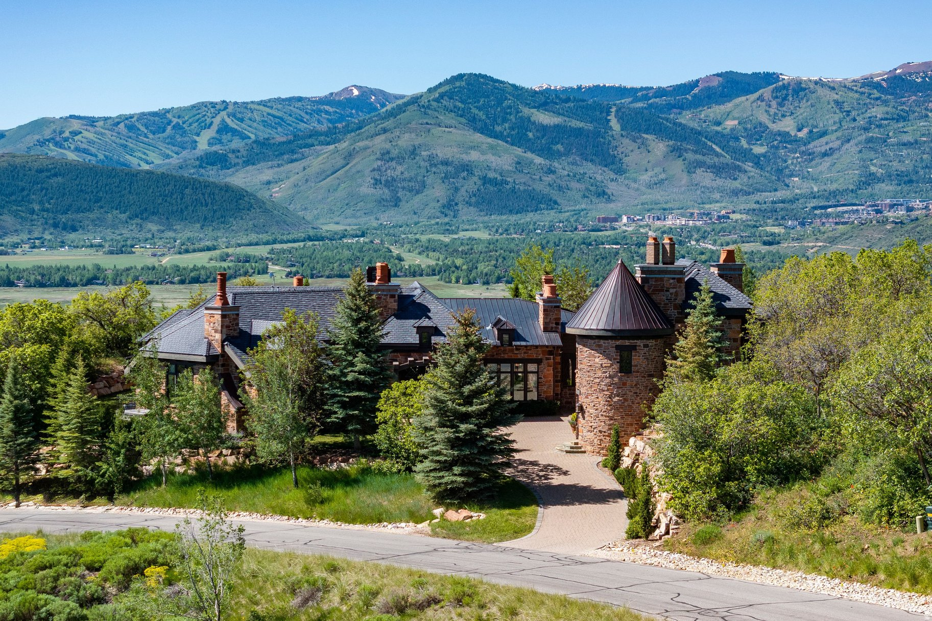 This beautifully constructed mountain estate sits just beyond the gates of Glenwild, perfectly positioned on 1.8 acres with sweeping views of Deer Valley Resort and the esteemed Glenwild Golf Course. Designed by Michael Upwall, this property was inspired by a refined Scottish hunting lodge and embodies a timeless Ralph Lauren aesthetic with rich textures, curated finishes, and impeccable craftsmanship. The grand entry is framed by hand-carved double doors with beveled glass that open to soaring ceilings, dramatic wood beams, statement lighting, and walls of windows perfectly capturing the mountain vistas. Designed for seamless main-level living and both intimate and grand entertaining, the great room centers around a dramatic fireplace with stone surround and herringbone brick, flowing effortlessly into the formal dining space and quiet reading nook. The chef's kitchen serves as the true heart of the home offering abundant prep space, a French La Cornue range, Wolf appliances and generous island seating. Accented by a highly functional butler's pantry ideal for catering or craft space with additional laundry facilities. A secondary living room with stunning leaded glass windows and its own fireplace provides flexibility for formal or informal living tucked away just beyond the kitchen. The executive office is perfectly appointed with oxblood ceilings, wood beams, custom built-ins, brass sconces, a stunning stone fireplace and a rich paisley wall covering creating a regal and dramatic workspace. Retreat to a primary suite that is both generous and serene, featuring custom wood paneling, a custom fireplace, spa-like bath with custom closets that provide ultimate organization and convenience with a hidden washer and dryer. Two additional main-level suites include a second primary option with a private deck, hammered copper soaking tub and stained-glass accents, while the third bedroom offers a charming window seat with built-ins and a thoughtful en suite bath. This property offers incredible cohesion with the surrounding grounds, with nearly every room opening to expansive paver decks designed for lounging, dining, and entertaining, complemented by mature landscaping and a flat lawn yard with panoramic mountain views. Outdoor features include multiple fireplaces, space for an outdoor kitchen, traditional bronze lanterns and copper gutters. Above the three-car garage sits a fully equipped guest residence with vaulted ceilings, full kitchen, dining area, private deck, gas fireplace, clawfoot tub, separate bedroom suite, and a hidden children's bunk nook behind Dutch doors. A cedar sauna and adjacent three-quarter bath add additional luxury. Additional highlights include a heated driveway, large garage with storage and epoxy floors, garage floors. central vacuum, slate-inspired metal and tile roof and thoughtful positioning set back from the road for privacy while maintaining easy gate access. Enjoy the ultimate in privacy and convenience with the guard-gated Glenwild Golf Club lifestyle providing world-class golf, spa, dining, and fitness amenities, all less than 30 minutes from downtown Salt Lake City and the international airport.