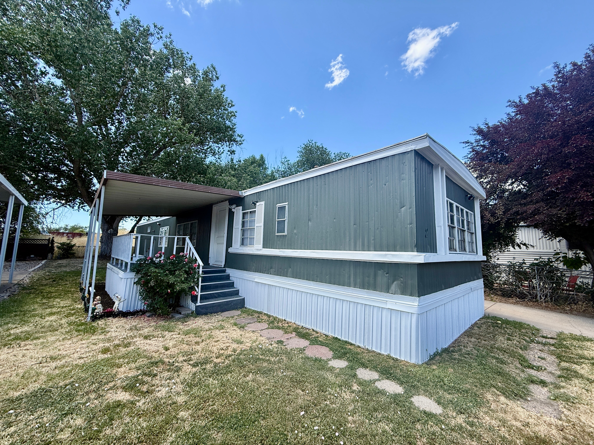 Charming and affordable mobile home offering a bright, functional layout with comfortable living spaces throughout. The open kitchen features black cabinetry, light countertops, stainless steel refrigerator, gas range, and updated flooring, with easy flow into the main living area. The spacious living room offers wood-look flooring, large windows giving warmth and character. Multiple bedrooms provide flexible space for sleeping, office use, hobbies, or storage. The home also includes a full bathroom/laundry combo with washer and dryer included, plus an additional half bath for added convenience. Outside, enjoy a covered porch entry, driveway parking, mature trees, and a manageable yard space. A great opportunity for affordable living with room to make it your own!