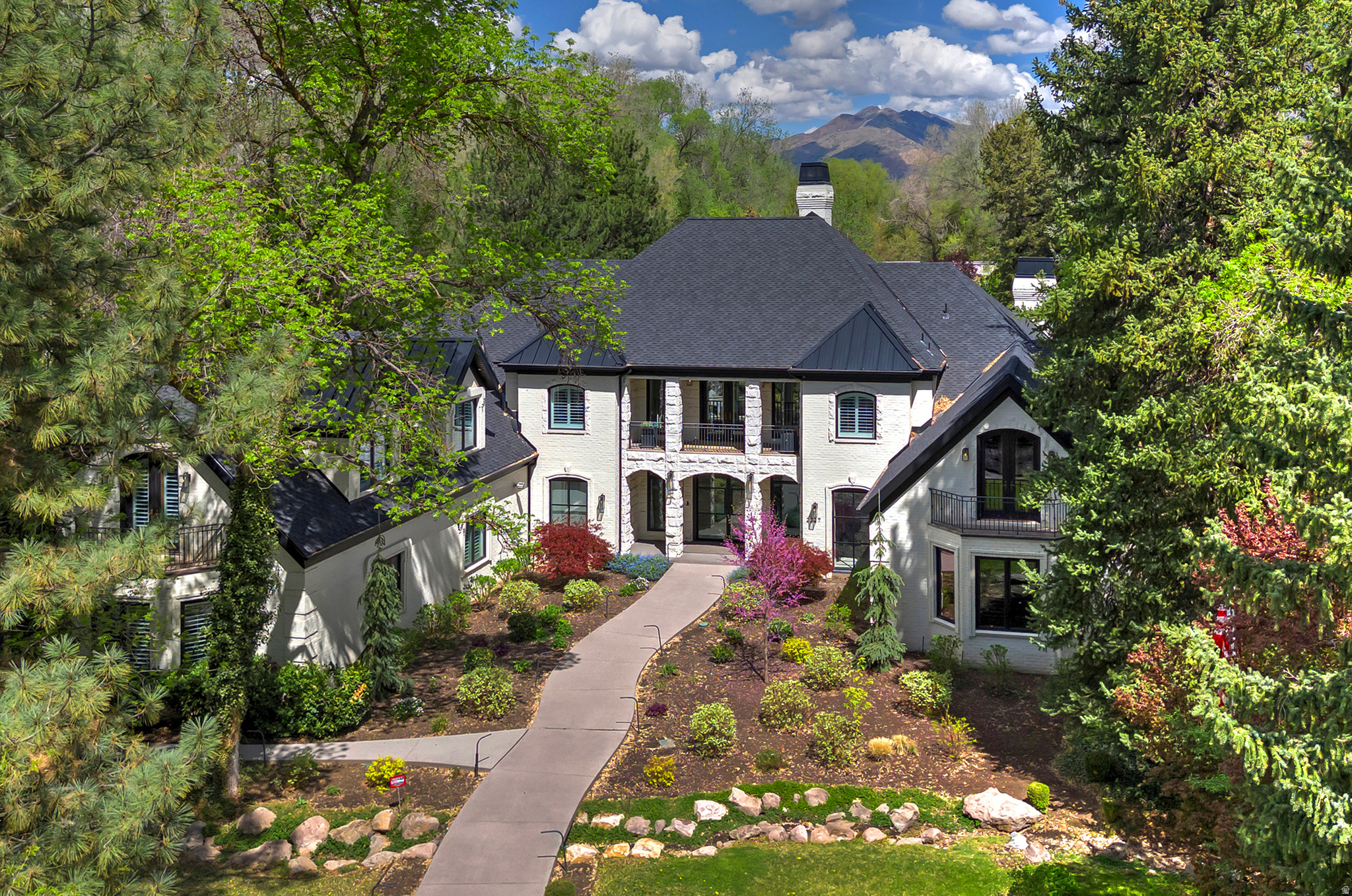 Gracefully set within one of Holladay's most coveted and serene enclaves, this gated estate is a masterful expression of modern elegance where grand, light-filled interiors meet the tranquility of lush, private grounds just shy of an acre. Reimagined to the highest standard and quality, the home showcases rich wood flooring, statement fireplaces, and a breathtaking chef's kitchen that anchors the expansive great room, designed for both sophisticated entertaining and effortless daily living. Walls of glass invite the outdoors in, creating a seamless transition to resort-inspired grounds featuring a saline pool, spa, outdoor kitchen, and a picturesque stream with cascading waterfall. The main-level primary suite offers a refined retreat with vaulted ceilings, a fireplace, and a spa-caliber bath complete with soaking tub and steam shower. A richly appointed library with custom built-ins adds warmth and distinction. Upstairs, a lofted gallery connects beautifully appointed ensuite bedrooms and additional living spaces, while the walkout lower level is designed for leisure, featuring a theater, game room, wet bar, and direct access to the grounds. A heated 4 car garage, circular drive, advanced security, and integrated smart home technology complete this exceptional offering-where privacy, sophistication, and timeless design converge.  Minutes from world class skiing, renowned medical facilities, hiking, biking and fine dining.