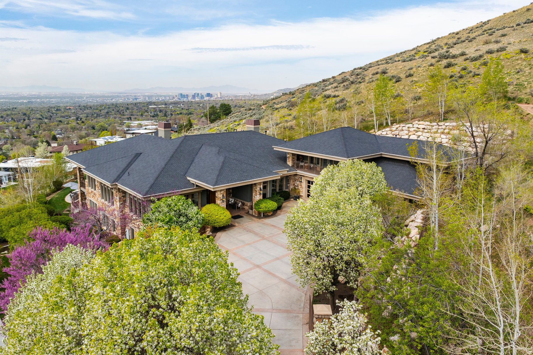 Perched on an exceptionally rare East Bench property this estate offers sweeping, unobstructed views across the entire Salt Lake Valley. The Contemporary Craftsman blends the warmth of a family retreat with the stature of a true legacy property. Set high on the East Bench foothills in a serene, park-like setting, the home offers remarkable privacy while remaining minutes from freeways, the University of Utah, downtown, and nearby ski resorts.  A gated, tree-lined drive leads to a residence defined by timeless craftsmanship-rich inlaid wood floors, soaring ceilings, refined moldings, and walls of windows that flood the home with natural light. Thoughtfully designed spaces invite both formal and casual gatherings, anchored by a spectacular double-island kitchen that serves as the heart of the home.  The lower level, a full walkout, offers expansive living and entertaining spaces: a theater, secondary kitchen, family and dining areas, a second laundry room, and abundant storage. The home features 6 ensuite bedrooms and 8 total baths, including a luxurious primary suite and a private upstairs guest quarters complete with full kitchen and a balcony facing Mt. Olympus.  Wraparound covered decks on both levels frame mesmerizing sunsets, sparkling city lights, and panoramic views in every direction. The outdoor spaces include a resort-style pool, separate hot tub, and mature landscaping designed for year-round enjoyment.  This property is a rare opportunity to own one of the most distinguished homes in the Salt Lake Valley-where unmatched views and exceptional design come together in perfect harmony.