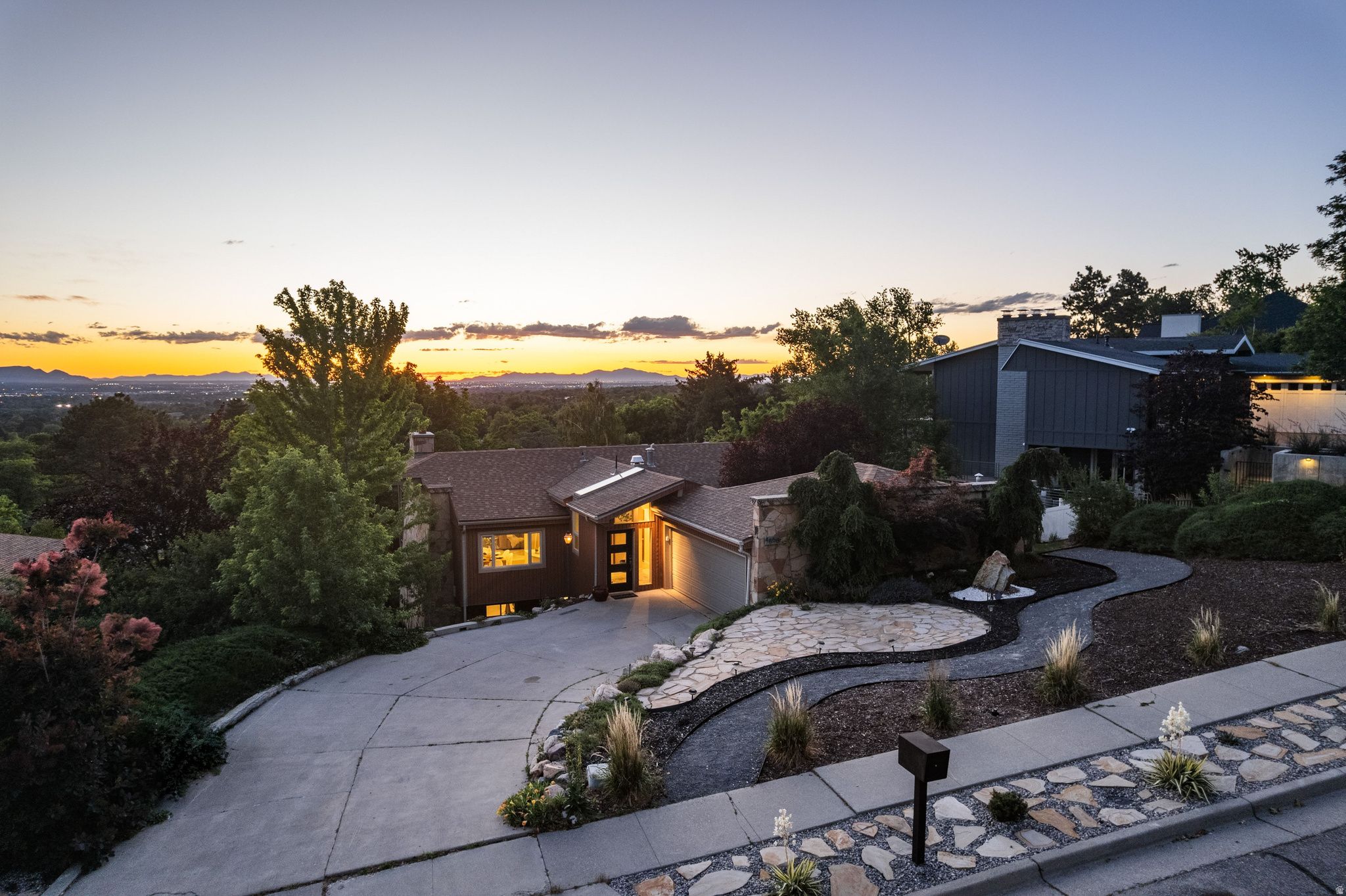 Perched in one of Holladay's most desirable neighborhoods, this thoughtfully updated mid-century modern residence captures the essence of elevated indoor-outdoor living. Expansive covered decking serves as a natural extension of the home, creating the perfect setting for entertaining, relaxing, and taking in the valley views and spectacular sunset skies.The home's contemporary mid-century character is highlighted by custom stonework that seamlessly ties together the interior and exterior spaces, while views of iconic Mount Olympus provide a stunning backdrop. Inside, recent updates blend modern comfort with timeless design, including beautifully remodeled upstairs and downstairs bathrooms, updated flooring in the main living areas, and new carpet in the upstairs bedrooms. Outside, the property has undergone a significant transformation. Extensive landscape improvements include a custom 50-foot retaining wall, complete yard regrading, new sprinkler and drip irrigation systems, lush sod, curated garden spaces, and an expanded outdoor living area with a custom concrete patio and private hot tub retreat. These enhancements dramatically increased the usability and enjoyment of the backyard while maintaining a low-maintenance xeriscape aesthetic in the front yard overlooking the Wasatch Front. Systemic upgrades include a new HVAC system, tankless water heater, upgraded garage door operating system, Ring security system, updated water service line from the street, and recent roof repairs. Fresh paint throughout further enhances the home's turnkey appeal. Exceptionally maintained and meticulously cared for, this residence offers a rare opportunity to own a true mid-century modern retreat where architectural character, thoughtful improvements, and one of Holladay's most sought-after locations come together beautifully. Finally a home that reflects your style!