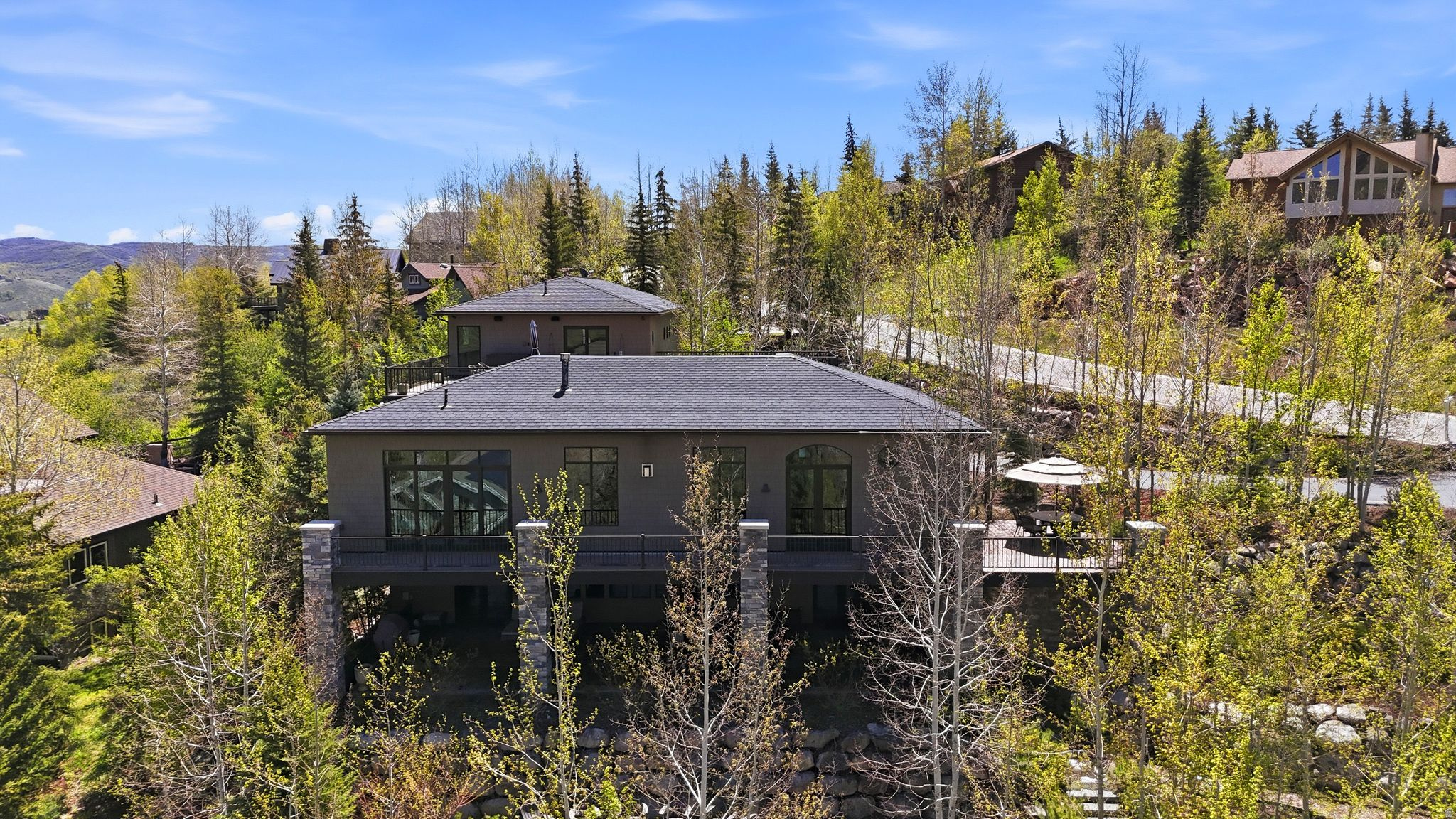 Tucked away on 1.35 private acres in the heart of Jeremy Ranch, this custom mountain residence delivers a rare combination of architectural sophistication and effortless livability. Designed with a modern mountain aesthetic, the home embraces its surroundings through generous glass, elevated ceilings, and a flowing layout that connects interior spaces to the outdoors. The primary suite on the main level creates an ideal everyday retreat, while two private ensuite bedrooms upstairs provide comfortable separation for guests or family. The lower level introduces exceptional flexibility with a fully self-contained apartment suite spanning approximately 2,000 square feet, complete with its own kitchen, fireplace, expansive patio, and a multi-purpose room suited for additional sleeping space, recreation, or entertaining. Outdoor living is a defining element of the property, offering multiple destinations to enjoy the setting-from a rooftop deck with sweeping views to a sheltered patio with fireplace, a private porch designed for quiet evenings, and a wraparound deck ideal for hosting guests. Mature landscaping, established walking trails, and a built-in gas fire pit enhance the sense of privacy and connection to nature. Despite its secluded feel, the home is ideally positioned just minutes from Park City amenities and ski resorts, and approximately 30 minutes from Salt Lake City International Airport. This is a thoughtfully designed and exceptional mountain contemporary home that balances privacy, comfort, and convenient access-an uncommon opportunity in one of the area's most desirable communities.