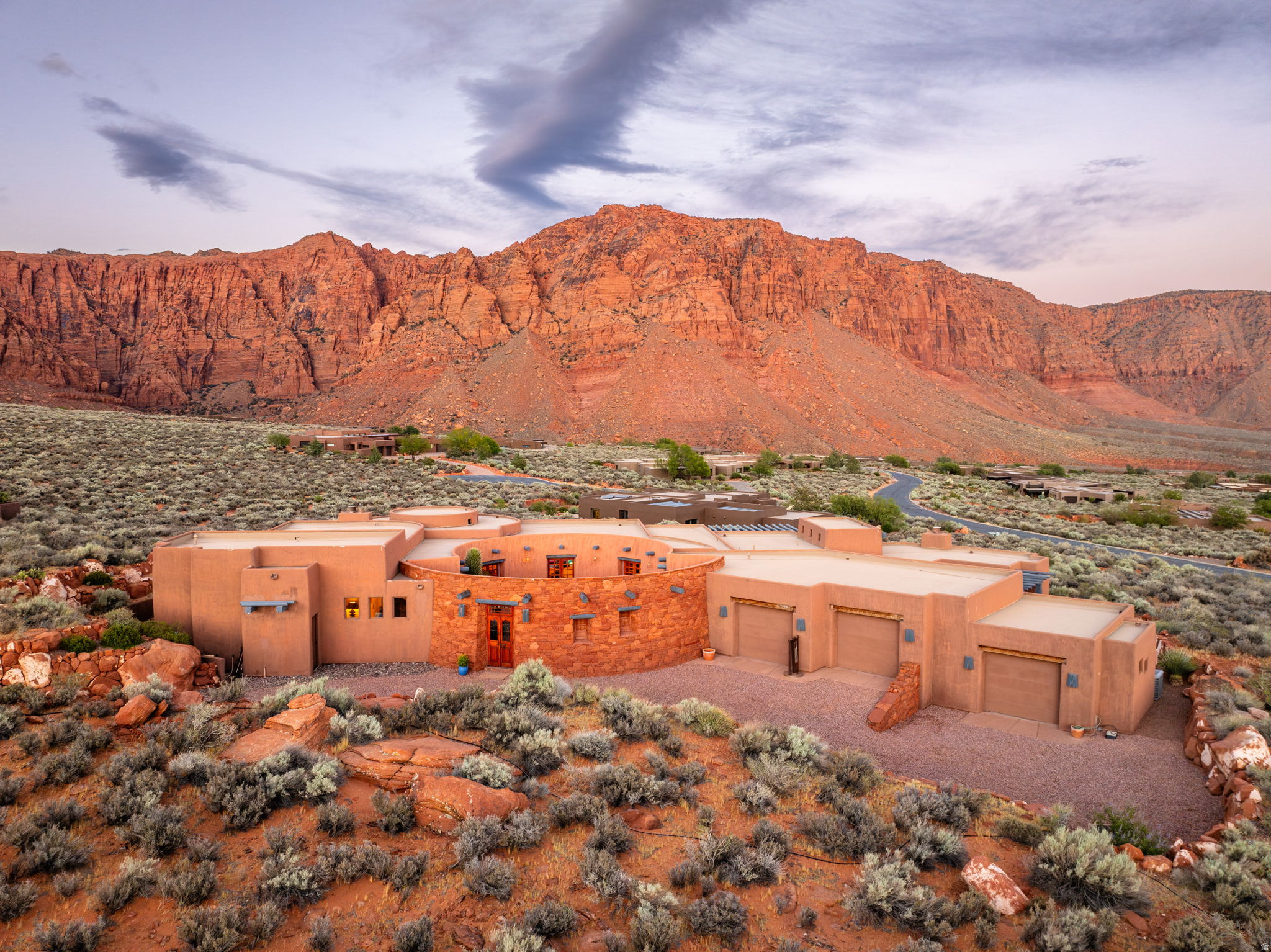 A sculptural Southwestern masterpiece set directly against the red cliffs of Ivins, where the architecture and landscape are one. The circular great room is wrapped in floor-to-ceiling windows with unobstructed red mountain vista views, a kiva fireplace, exposed wood beam ceiling and hardwood floors. The kitchen features custom cabinetry, granite countertops, and a stunning hand-painted tile mural backsplash. The primary suite offers a fireplace, custom hand carved wall accents, and red rock views from every angle. A fully attached casita with its own kitchen, living area, and private entrance adds incredible flexibility. Outside, the pool and patio are framed by open desert and canyon walls. 3-car garage, secluded setting, and unmatched privacy, yet it remains just minutes from Ivins and St. George amenities.