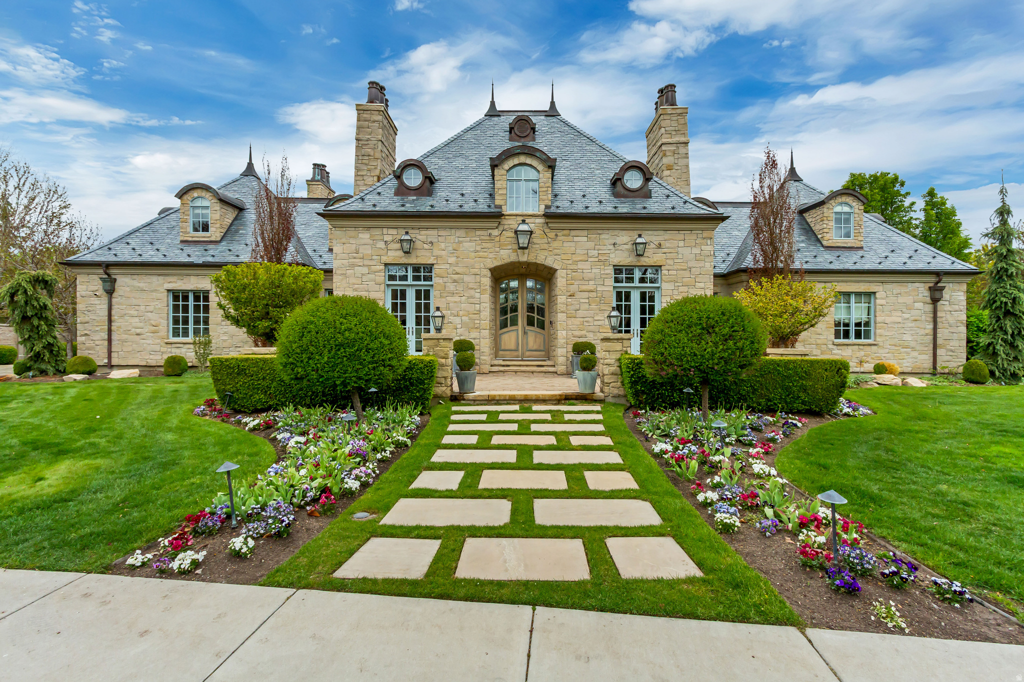 Inspired by the timeless charm of Southern France, this beautifully maintained residence blends old-world elegance with the warmth and livability of a true cottage retreat. From the moment you step inside, you're met with soaring ceilings, a stunning staircase, and rich wood beams and finishes that carry character throughout every space. Laundry on every level, multiple grand fireplaces and thoughtfully curated lighting add both scale and ambiance. The kitchen is designed to impress and perform, featuring dual sinks, double dishwashers, an oversized pantry, and a striking marble island that anchors the space for both everyday living and entertaining. The fully finished lower level expands the home's versatility with a private entrance, full kitchen, theater room complete with a built-in popcorn station, gym, and a dedicated craft and safe room. A rare 5-car garage is complemented by a private mother-in-law suite, offering flexibility for guests or extended living. Set within the highly coveted gated Stone Gate community in the Provo River Bottoms, this home offers a lifestyle that's hard to replicate. Surrounded by towering mature trees, peaceful walking paths, and access to the Provo River trail system, the neighborhood is known for its private, tucked-away feel while still being incredibly connected. Enjoy exceptional community amenities including a resort-style pool, pickleball courts, sand volleyball, basketball courts, and endless opportunities for biking, walking, and outdoor recreation. Located just minutes from Provo Canyon, Riverside Country Club, BYU, UVU, and some of the area's best hiking and trail systems, the setting perfectly balances luxury, recreation, and convenience. A home that delivers both presence and comfort, this is one you simply don't come across often. Buyer/Buyer's Agent to verify all information.