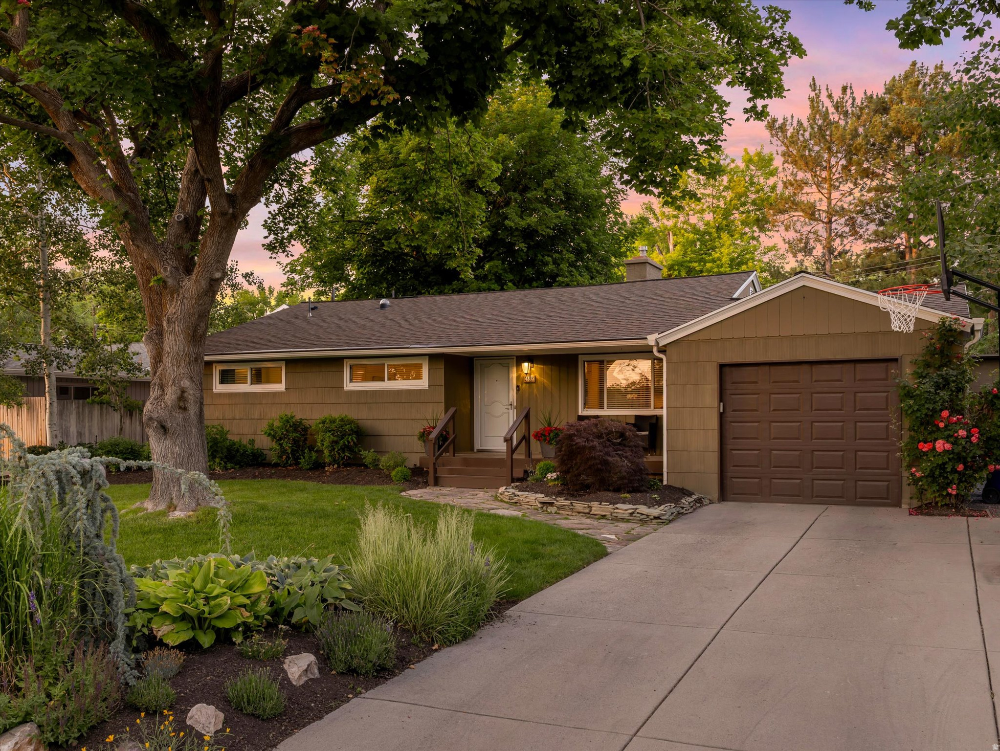 Welcome to this Holladay treasure. From the moment you arrive, the mature old-growth trees, lush professional landscaping, and expansive lot signal that this is something special. Step inside and be greeted by gorgeous original hardwood floors that flow through the main level, punctuated by a show-stopping herringbone pattern in the fully remodeled kitchen. The kitchen is outfitted with sleek stainless steel appliances (all included), a gas range, and stylish cabinets with quartz countertops. Natural light pours through newer windows, filling every room with warmth throughout the day. Cozy up by the mid-century fireplace and watch the seasons through the newer wall of windows in the back of the house. The main floor offers three bedrooms, a rare find for a home of this era, along with one and a half baths. The finished basement adds a large rec room, two additional bedrooms, and a three-quarter bath. There is also a large laundry area and extra storage space. But the true star of this property is the yard. The outdoor space is extraordinary, a genuine sanctuary with towering mature trees, beautiful established landscaping, and a huge Trex deck perfect for entertaining or simply unwinding at the end of the day. Practical updates include furnace, AC, and roof, and vinyl windows. The attached one-car garage adds everyday convenience, and the home's unbeatable location puts you within walking distance of the beloved Holladay parks, shops, restaurants, and easy access to Olympus High School and Olympus Junior High.