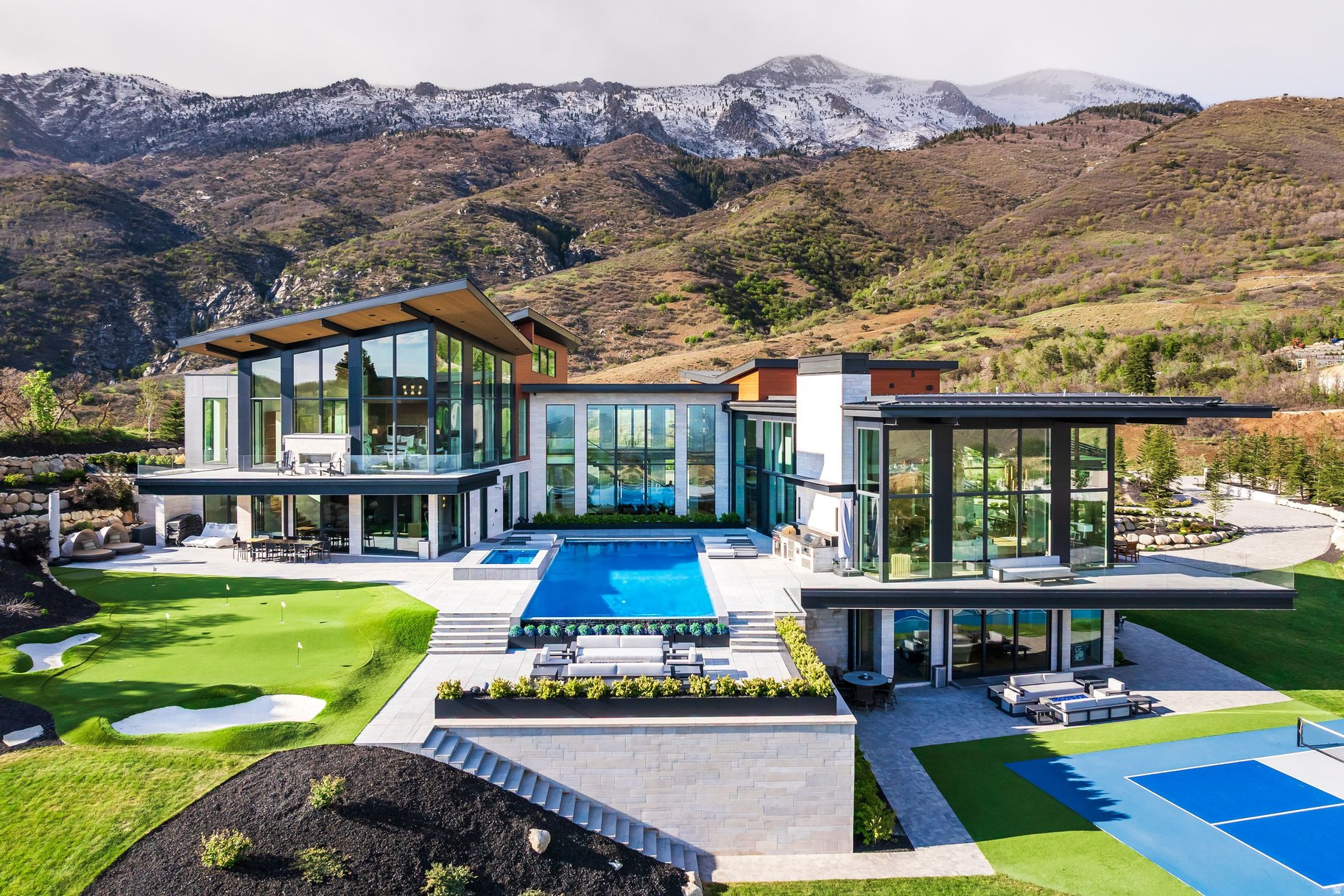 Positioned on one of the premier homesites in Three Falls, this extraordinary modern estate combines dramatic architecture, expansive living spaces, and panoramic views that stretch across Utah Valley, Utah Lake, and the surrounding Wasatch Mountains. Floor-to-ceiling glass, soaring ceilings, steel accents, and warm natural materials create a striking architectural statement while maintaining a strong sense of comfort and livability throughout the home. Designed for both large-scale entertaining and everyday living, the main living spaces open seamlessly to resort-style outdoor amenities that include a stunning infinity-edge pool and spa, expansive patios, multiple gathering areas, a putting green, sport court, and beautifully landscaped grounds. The kitchen is equally impressive with custom cabinetry, high-end appliances, a separate prep kitchen, and extensive storage. The primary suite occupies its own remarkable retreat with dramatic mountain views, a statement fireplace, spa-inspired bathroom, boutique-style closet, and private sitting area. Additional features include multiple guest suites, a striking floating staircase, elevator, executive office, golf simulator, full indoor sport court with climbing wall, fitness center, lower-level entertainment spaces, and oversized garage capacity with extensive storage. Every detail throughout the property reflects exceptional craftsmanship, thoughtful design, and a level of quality rarely found along the Wasatch Front.