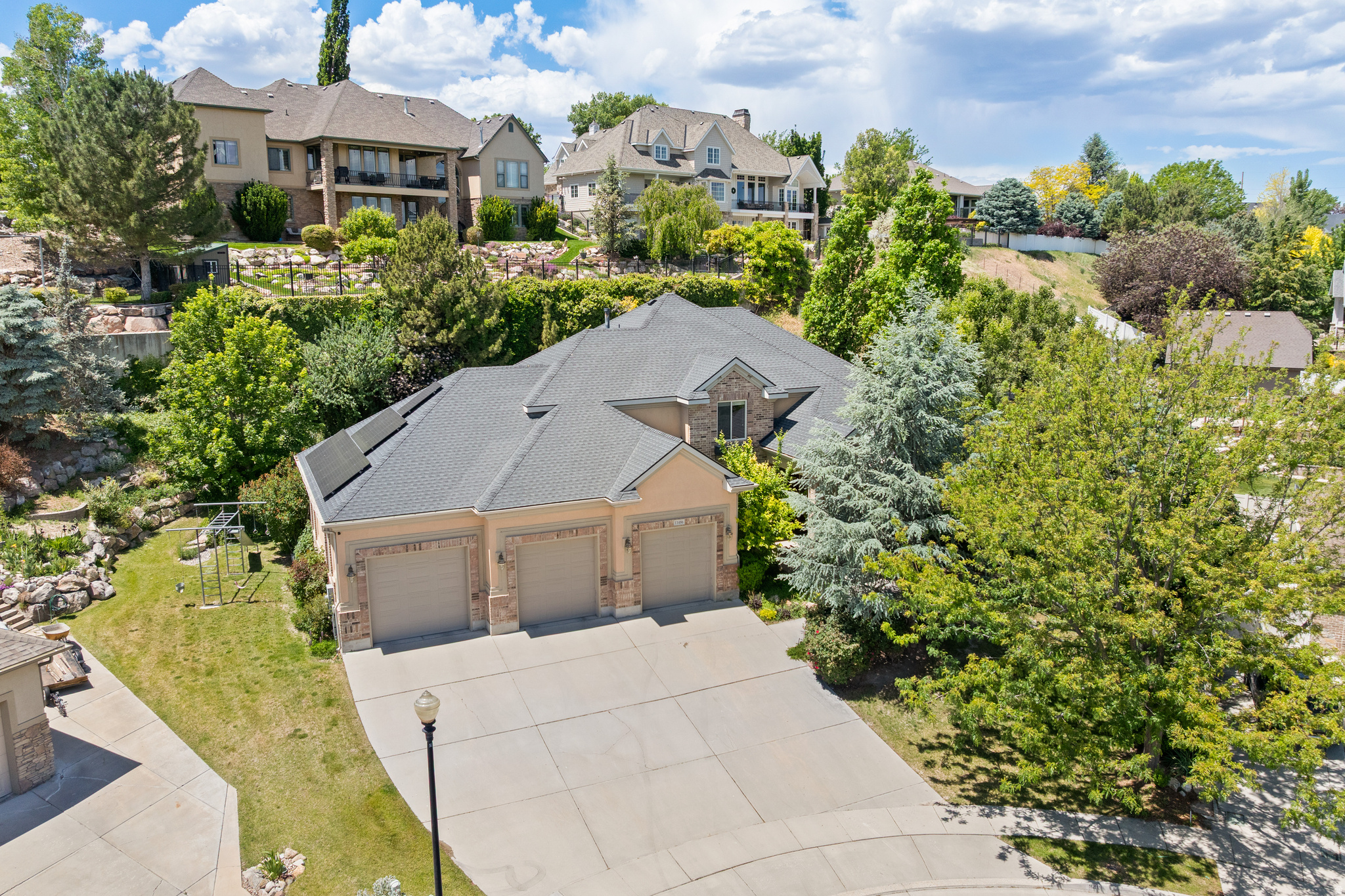 Welcome to this stunning, expansive residence tucked away on a quiet cul-de-sac in one of South Jordan's most sought-after neighborhoods. Perfectly positionedagainst a serene hillside, the property offers exceptional natural privacy amid lush, mature landscaping. Featured in the Parade of Homes when built, this impressive property showcases timeless design, quality craftsmanship, and spacious living throughout.  The main level features an open-concept kitchen, dining area, and family room with a gas fireplace and walks out to a spacious deck. The kitchen offers custom cabinetry, Silestone countertops, a large island, Wolf double ovens, and a gas cooktop. The main level also includes a living room and flex room, creating additional living and entertaining space.  Upstairs, the primary suite includes a gas fireplace, walk-in closet, private covered deck, and ensuite bathroom with two vanities, jetted tub, and separate shower. Two additional bedrooms share a Jack-and-Jill bathroom, and an office with soaring ceilings, large windows, built-in custom cabinetry and desk. Upstairs laundry adds convenience.  The lower level includes a spacious family room with a full second kitchen, two bedrooms, a full bathroom, and a large unfinished room with extra ceiling height. This area is ideal for guests or mother-in-law living. Also includes a large storage room.  The backyard offers exceptional privacy with no direct rear neighbors, expansive deck space, and an in-ground hot tub surrounded by a beautiful hillside backdrop. Additional outdoor features include an in-ground trampoline, covered outdoor dining area with built-in heater, swingset, and multiple spaces for entertaining and relaxing.  Rare 5-car garage with exceptional space for vehicles, recreational gear, storage, or a workshop. Additional highlights include solar panels, exterior security cameras, and Ring doorbell system.  Conveniently located near shopping, dining, parks, schools, and freeway access.