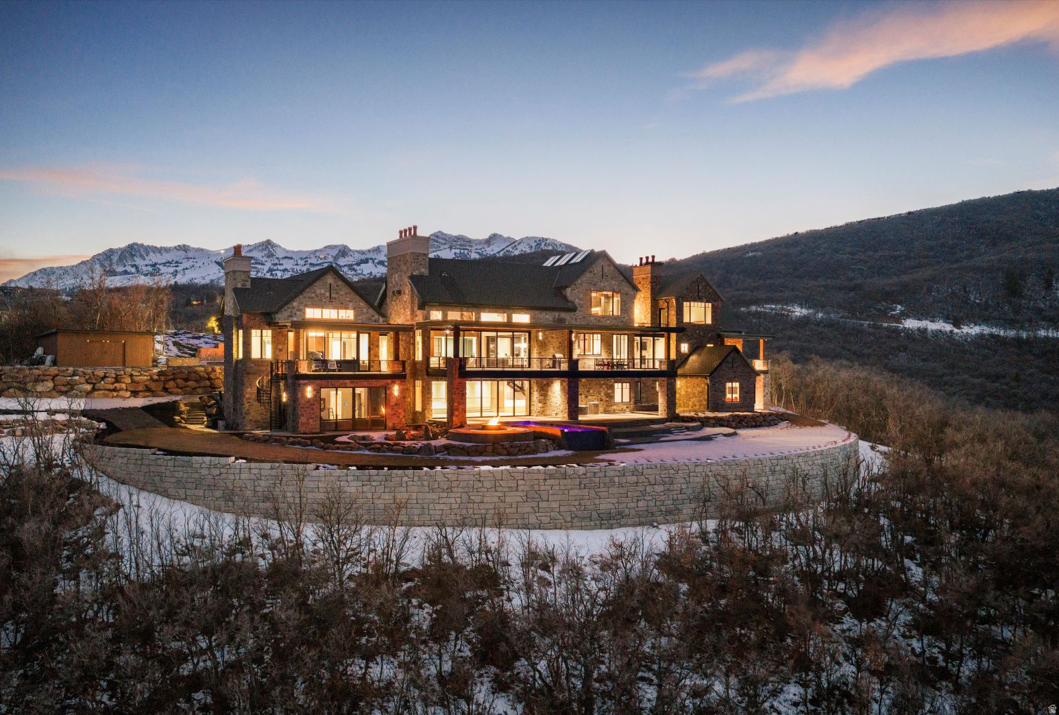 Rising above Ogden Valley on the premier lot within Legacy Mountain Estates, this once-in-a-lifetime 5.6-acre estate is a masterwork of scale, imagination, and precision. Spanning an extraordinary 18,700 square feet, the residence offers eight bedrooms and fourteen bathrooms, delivering uncompromising luxury at every turn. Arrival is nothing short of cinematic, framed by custom-landscaped grounds, cascading waterfalls, stone stairways, a reflection pond, and a dramatic porte cochere. From this unmatched vantage point, the estate commands truly one-of-a-kind panoramic views, an ever-changing masterpiece of mountain peaks, valley lights, and endless sky. Beyond its breathtaking setting, the property features amenities rarely found in private residences, including more than $1 million invested in a fully automated, professionally designed lighting, audio, and control system. With a multi-point security system, gated entry, and extensive camera coverage. For seamless indoor-outdoor living, the main level and primary suite open to expansive heated decks through automatic sliding accordion doors. Just ten minutes away lies world-renowned Snowbasin Resort, set to take center stage as a premier venue for the 2034 Winter Olympics, offering effortless access to championship skiing, dining, and Pineview reservoir, offering year-round adventure. A private one-bedroom casita provides additional space for guests, while an entire spa and wellness retreat awaits, featuring a massage house, steam shower, sauna, and dedicated gym. Hidden beyond the expected lies a secret passage leading to a meticulously crafted mine-inspired destination, home to a wine cellar, speakeasy, infinity cart viewing hall, and the showstopping 20,000-gallon lagoon theater. Here, water, light, and architecture converge through exterior-fed fountains, aqua-stage elements, balcony seating, and performance space. Rarely does a property of this scale, artistry, and provenance come to market. This is more than a home; it is a generational estate, an architectural landmark, and a singular mountain legacy.  An additional 3300 sq ft heated garage space. Square footage figures are provided as a courtesy estimate only. Buyer is advised to obtain an independent measurement.