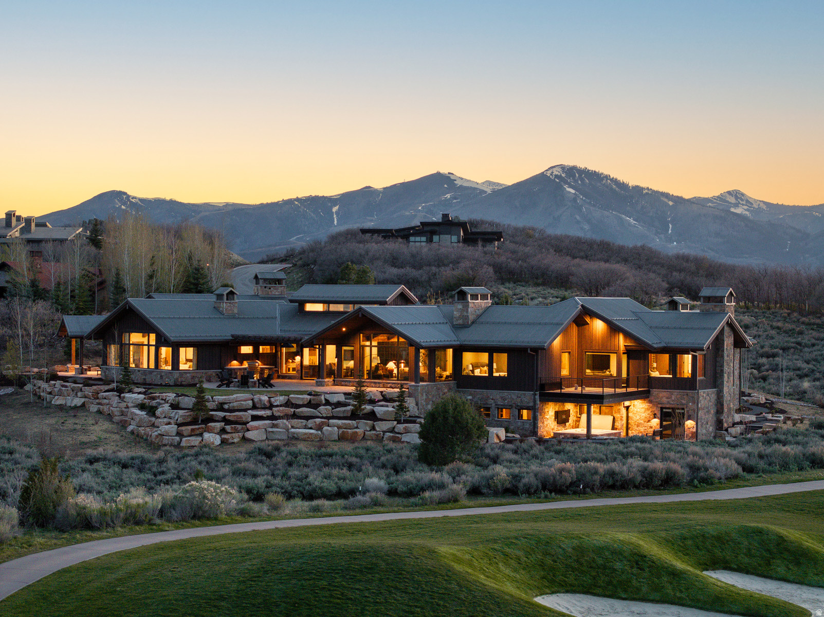 Set against the breathtaking backdrop of the Wasatch Mountains, this newly completed custom estate offers an extraordinary opportunity for elevated golf course and mountain living within the exclusive Talisker Club enclave of Tuhaye, just 15 minutes from downtown Park City. Perfectly positioned along the 6th, 7th, and 9th holes of the Mark O'Meara designed championship golf course, the property delivers a rare blend of serenity, privacy, and recreation. Ownership includes the option of full membership to the Talisker Club, granting privileged access to world class skiing via the Talisker Tower Club, immersive backcountry experiences at the Talisker Club Outpost, and exceptional dining at Courchevel Bistro on historic Main Street. The recent addition of the Hot Creek Cabin lodge in Empire Pass further enhances this already unparalleled mountain lifestyle. Never-before lived in, this thoughtfully designed estate rests on nearly 1.7 private acres and is ideally situated at the end of a quiet cul-de-sac. Within a 24-hour guard gated community, the home captures sweeping panoramic views of the golf course and surrounding peaks from nearly every room. A heated driveway ensures effortless year-round access, leading to a spacious motor court, multi-car garage, dedicated golf cart garage and a striking architectural arrival. Designed by the renowned Brighton Architectural Group, constructed by Landmark West, with interiors by Bond Design Company, the approximately 9,871 square foot home showcases exceptional craftsmanship and premium finishes throughout, as well as hand-selected designer furnishings that are included with the home. Inside, a dramatic foyer frames a direct sightline of the golf course and mountains beyond, setting the tone for the home's open, airy design. The great room serves as the centerpiece, featuring soaring vaulted and beamed ceilings, wall of windows, and an effortless flow onto dining room, the chef's kitchen and butler's pantry.  Designed to live like a single-level home, the primary suite is thoughtfully separated from guest accommodations. The primary suite is a private retreat with vaulted ceilings, expansive windows, and refined custom finishes. One office nook and one dedicated office, the latter with floor to ceiling windows, bespoke built-ins, and a striking black metal fireplace, offer an inspiring workspaces. Both the primary suite and main office open to a covered patio with uninterrupted golf course and mountain views.  The east wing hosts three additional bedrooms, each uniquely designed with en suite baths, connected by a welcoming shared living area that provides both comfort and privacy for guests.  Accessible via elevator or dual staircases, the lower level transforms into a private resort. Highlights include a spacious entertainment lounge, six custom built-in bunk beds, a state-of-the-art golf simulator, steam room, fitness center, and wine cellar with a brick barrel ceiling. Additional features include secure, custom-built safe room and approximately 1,035 square feet of storage, mechanical, and janitorial rooms.  Completing the estate are upper and lower laundry rooms, a mud room, and modern technology such as built-in audio, Samsung Frame TVs, and a Lutron smart home system controlling lighting, audio, and window treatments. Outdoor living is equally impressive, with expansive heated patios designed for year-round enjoyment, a built-in barbecue and entertaining area, and a luxurious in-ground spa, all set against a stunning alpine backdrop.  Just minutes away, Jordanelle Reservoir offers endless recreation, while shopping, dining, and entertainment in Park City and the emerging Deer Valley East Village are within easy reach.